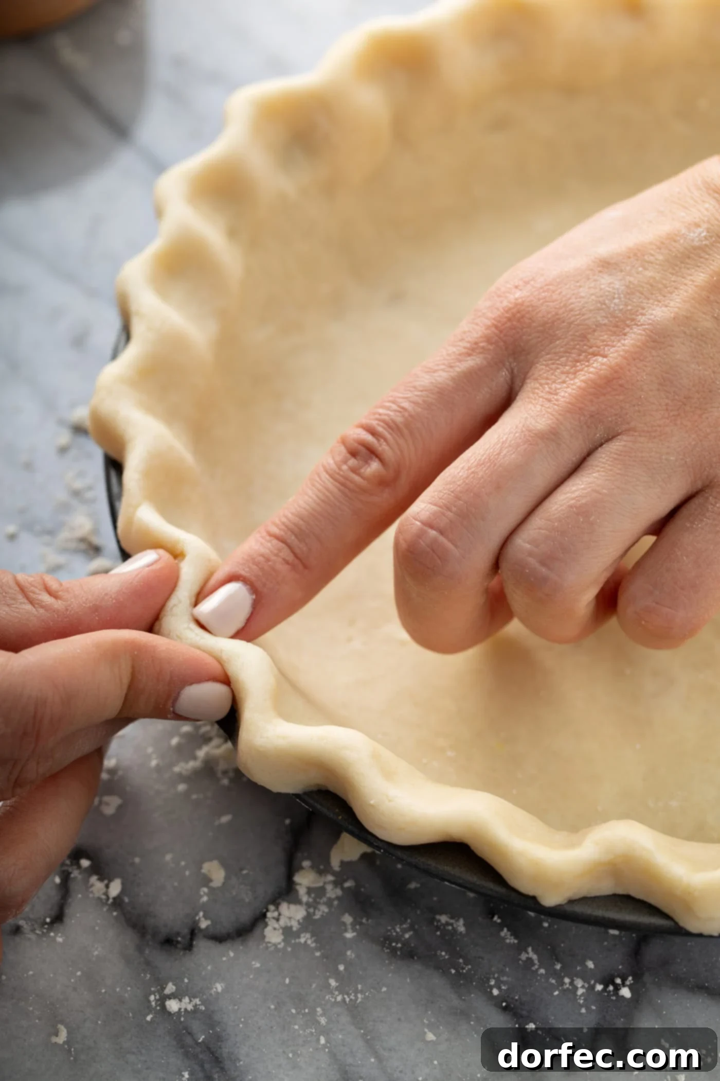 A pair of hands delicately crimping the edges of an uncooked pie crust, creating a beautiful decorative border.