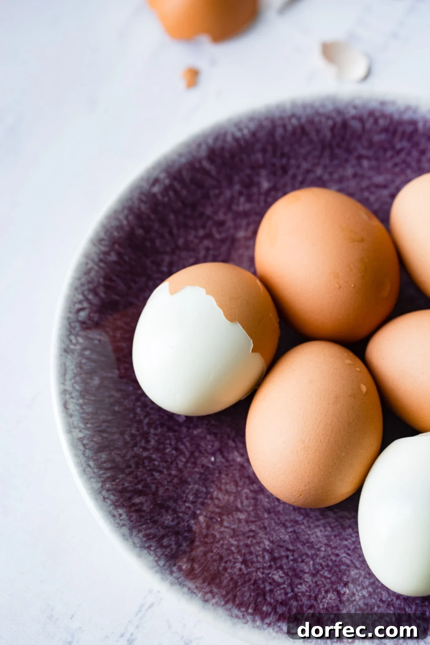 A plate with 6 brown hard boiled eggs. On egg is peeled and another egg is partially peeled.
