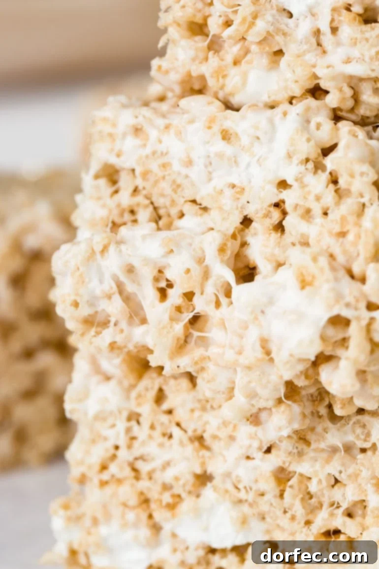 Extra Gooey Rice Krispie Treats 5 Three thick pieces of gooey Rice Krispie Treats, lovingly stacked and showing off their stretchy, melted marshmallow consistency, ready to be enjoyed.