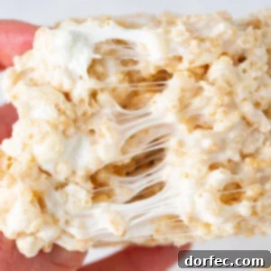 Close-up of a stack of three gooey homemade Rice Krispie Treats, displaying their thick, soft, and chewy texture with visible marshmallow pockets.