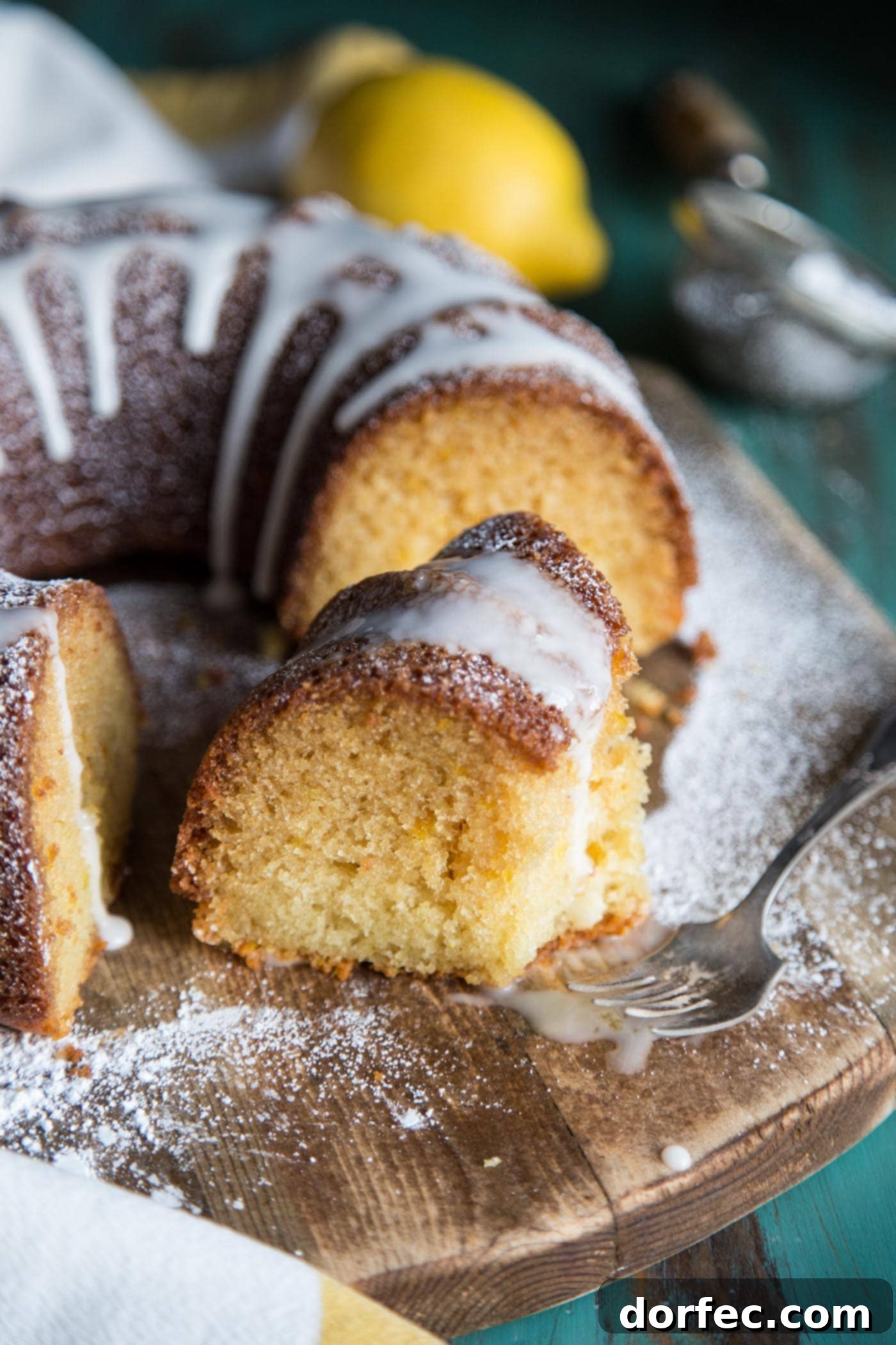 A slice of moist lemon bundt cake with glossy lemon glaze, ready to be served on a pristine white plate, capturing the light perfectly.