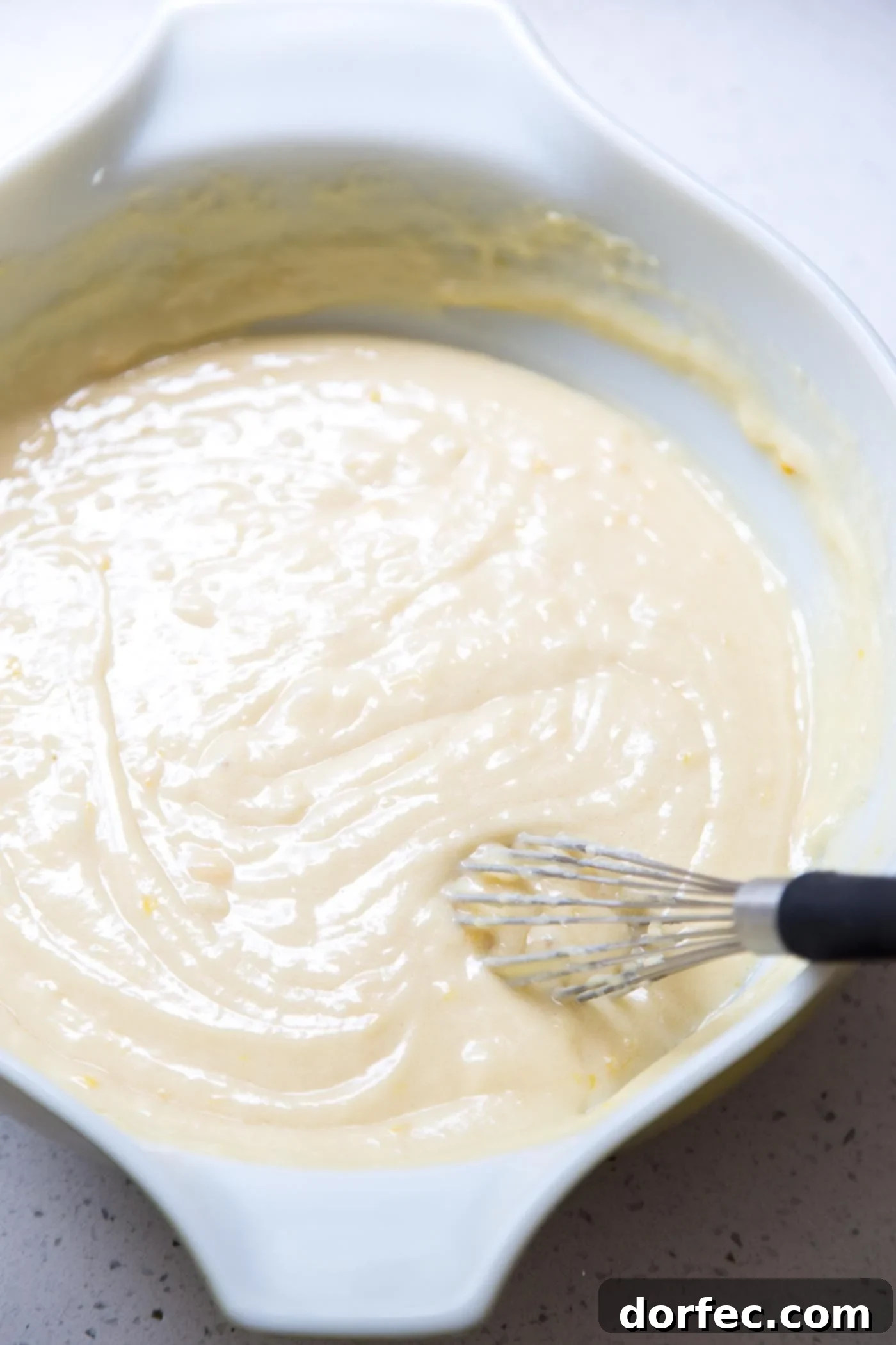 Rich, yellow lemon bundt cake batter swirling in a large glass mixing bowl, showcasing its creamy texture before baking.