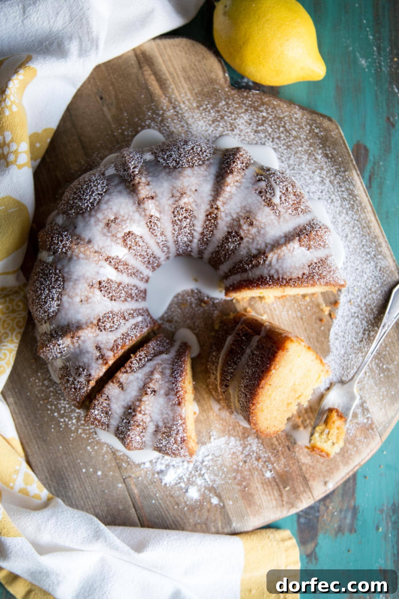 A beautifully glazed lemon bundt cake, decorated with fresh lemon slices and a sprig of mint, resting on a rustic wooden board.