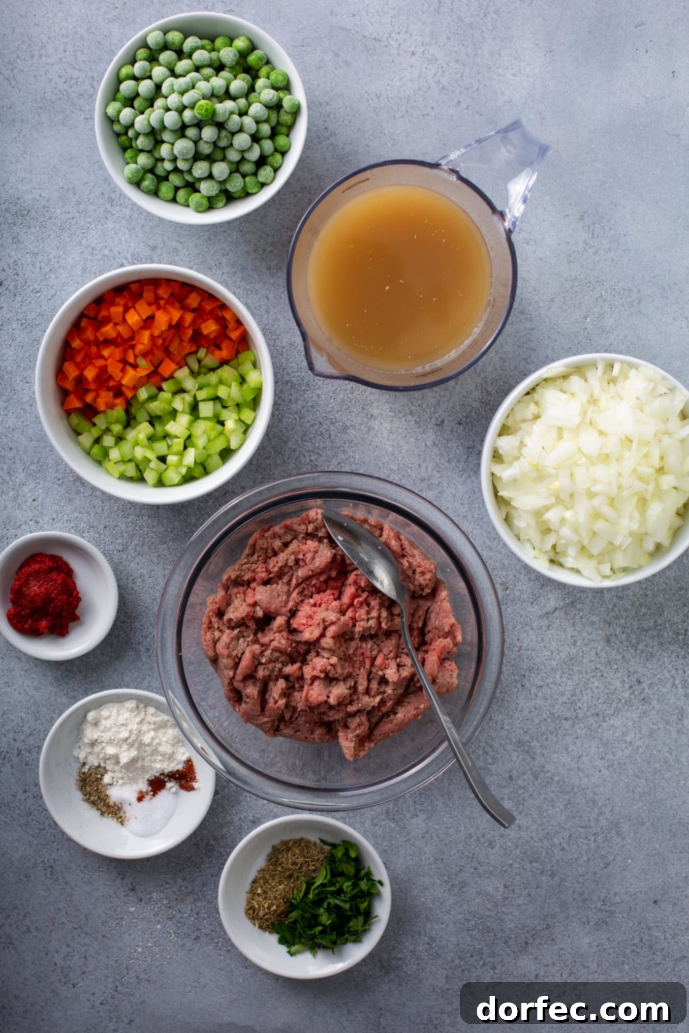 A table top with containers of ground beef, onions, chopped red and green peppers, spices, peas, and broth.