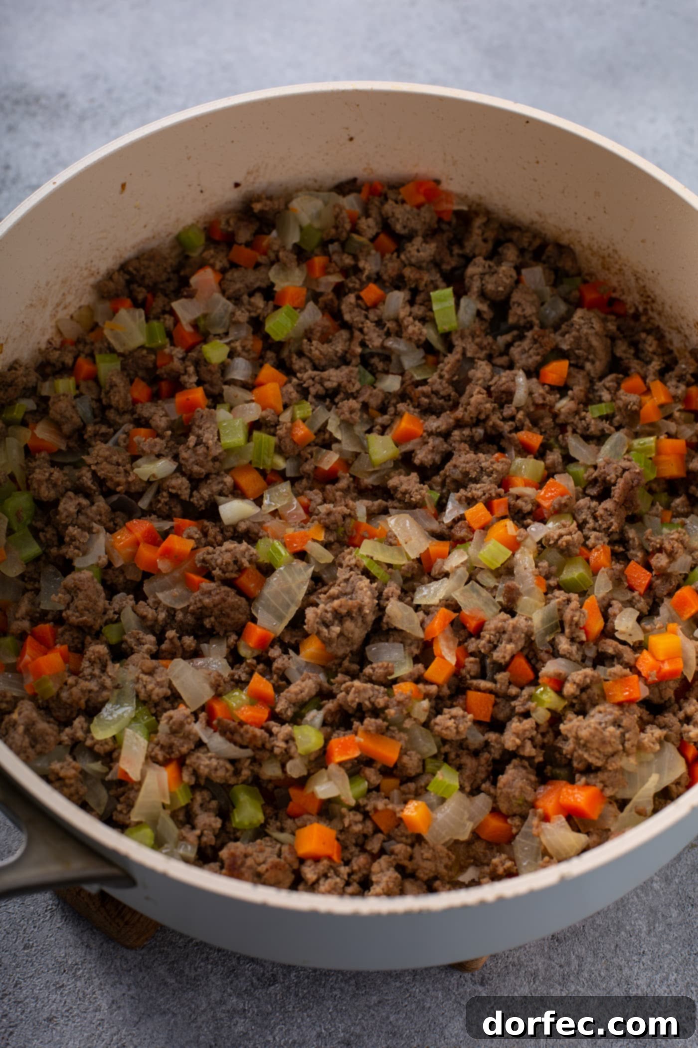 A casserole dish filled with browned ground beef, onions, peas, and carrots.