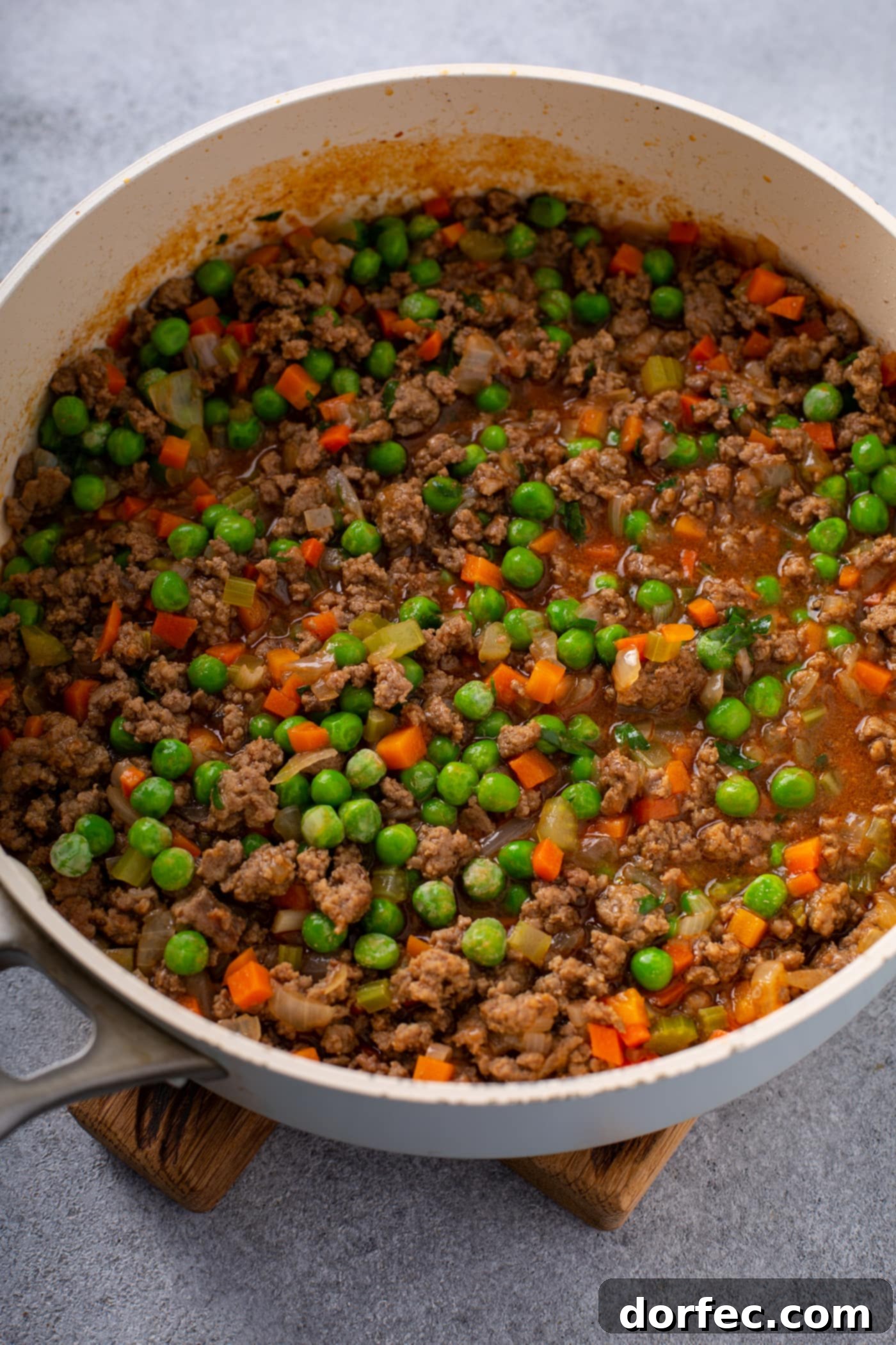 A casserole dish filled with browned ground beef, carrots, peas, onions and celery.