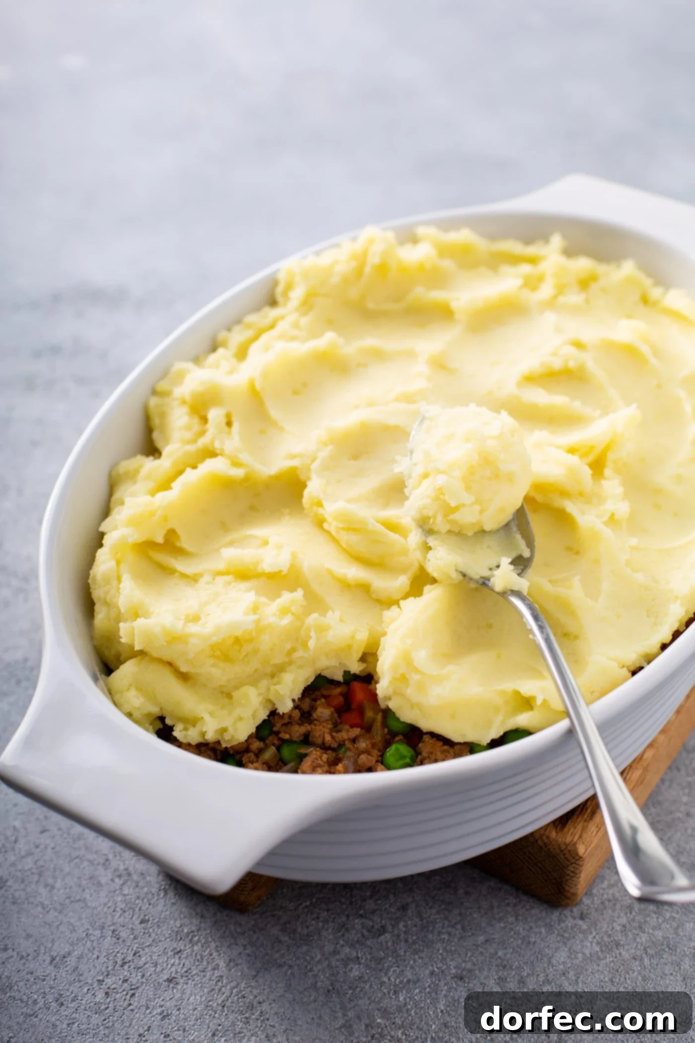 A casserole dish filled with shepherd's pie filling and topped with mashed potatoes. There is a spoon resting on top.