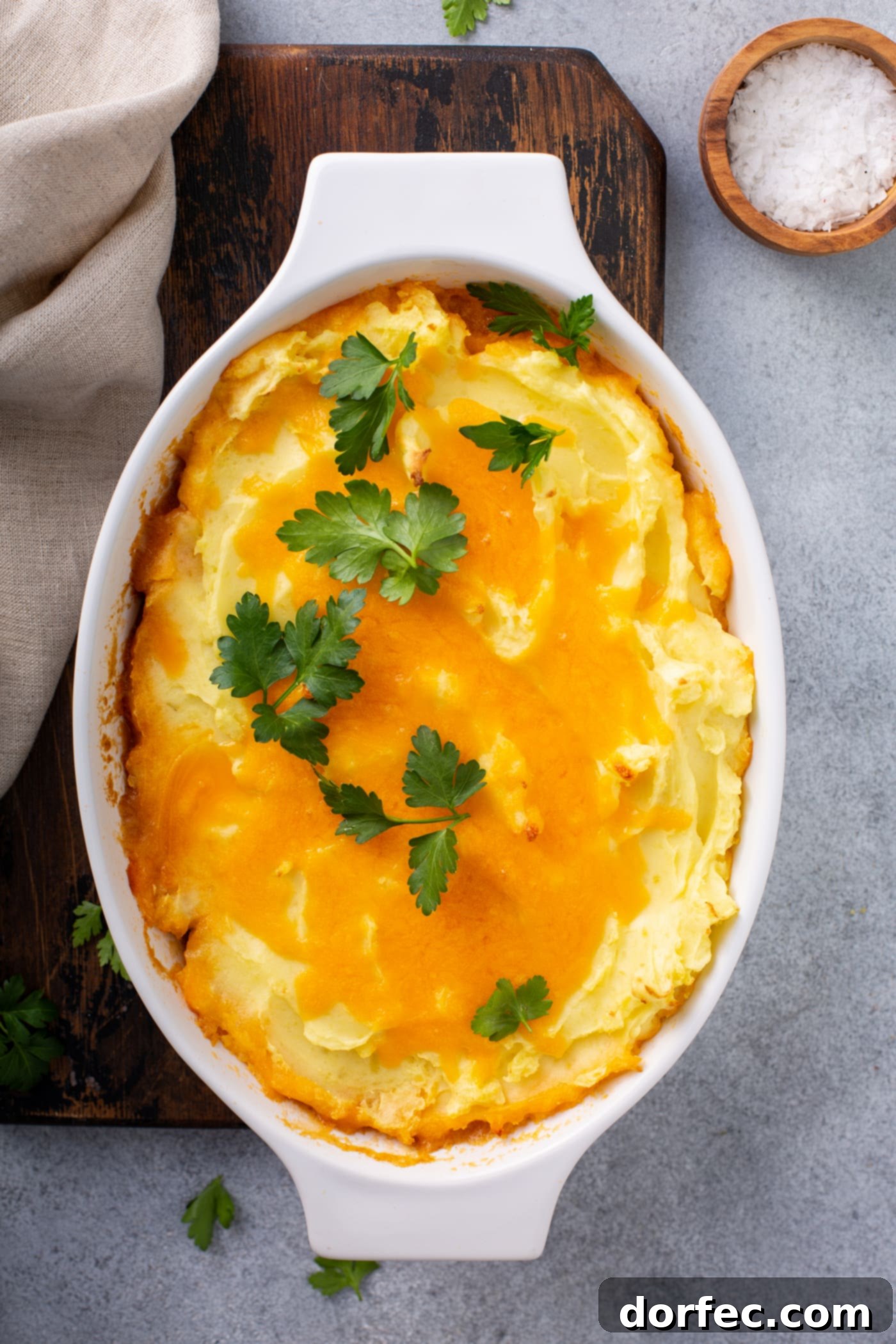 A casserole dish containing a baked shepherd's pie. It is topped with melted cheese and parsley leaves.