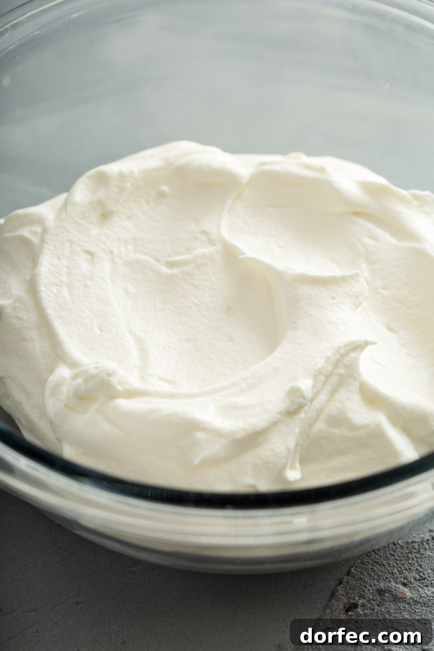 A pristine glass bowl is filled to the brim with perfectly whipped homemade cream, showcasing its irresistible lightness and fluffy texture.