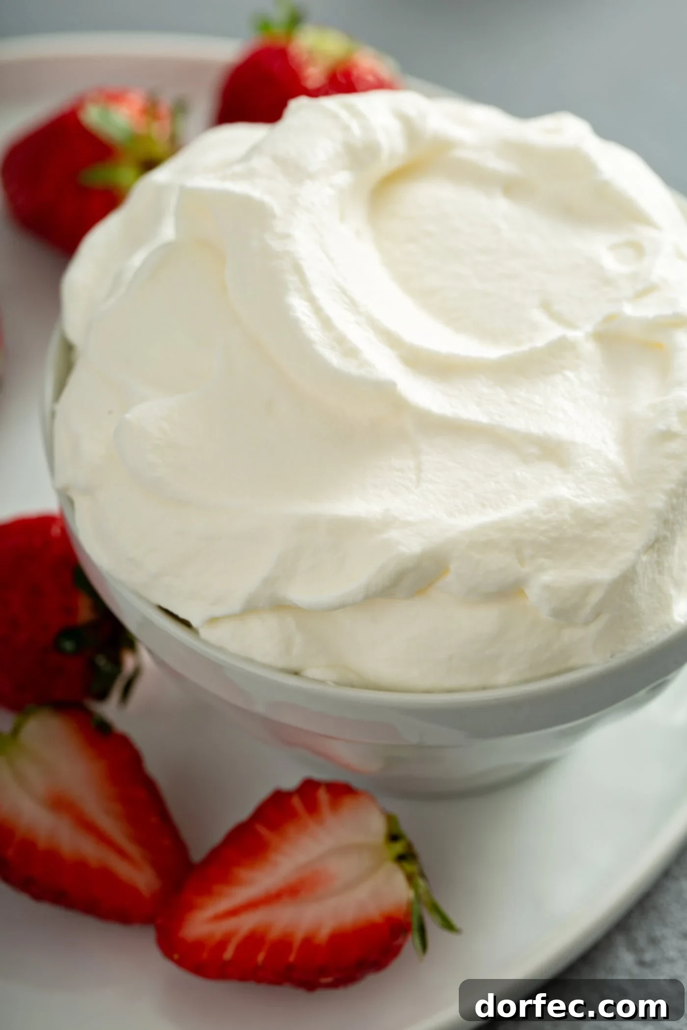 A rustic wooden bowl brimming with freshly prepared whipped cream is beautifully surrounded by an arrangement of whole, ripe strawberries, highlighting a perfect pairing for any dessert.