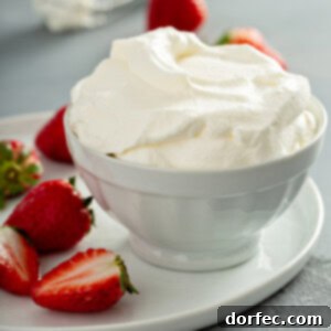 A bowl of whipped cream sitting on a plate with a few sliced and whole strawberries. There is a whisk and two strawberries in the background.