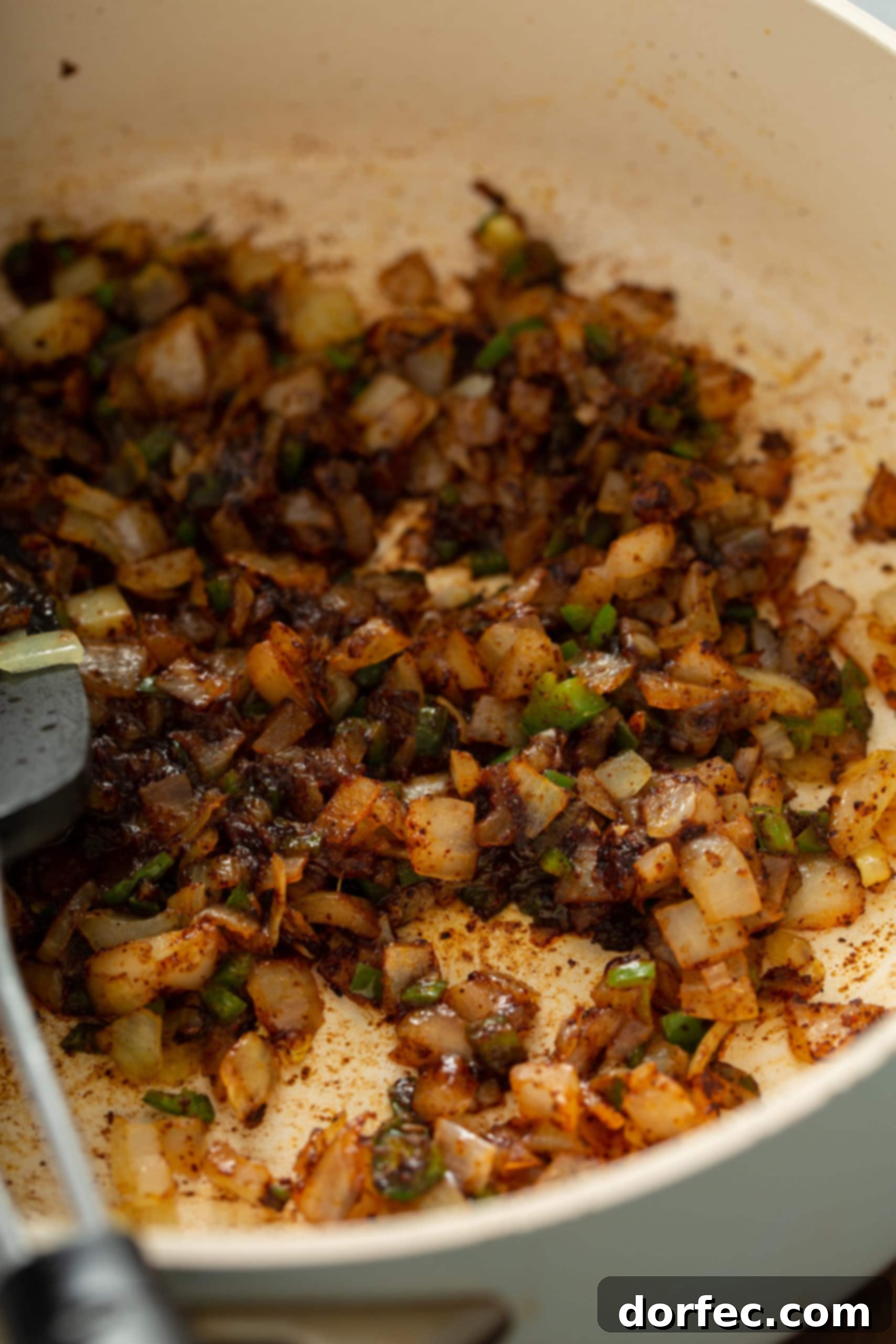 A stainless steel skillet showcasing a savory mixture of sautéed onions, jalapenos, and minced garlic, gently cooked to perfection, forming the aromatic base of the enchilada sauce.