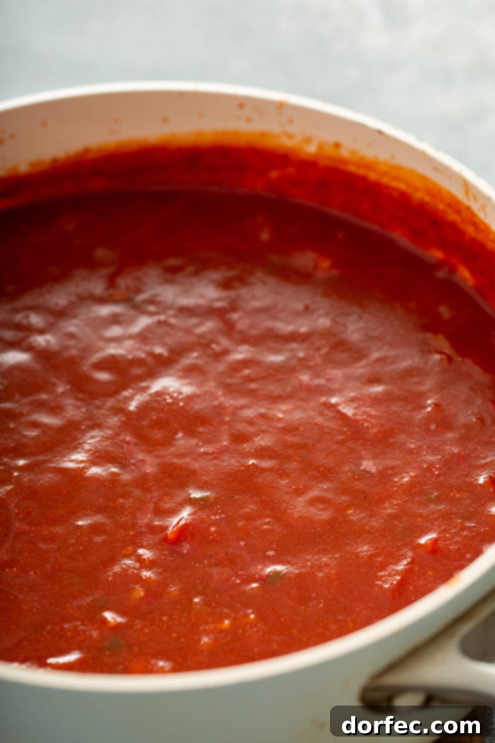 A glass container filled with rich, vibrant homemade red enchilada sauce, showcasing its smooth texture and appetizing color, ready for use in any delicious Mexican dish.