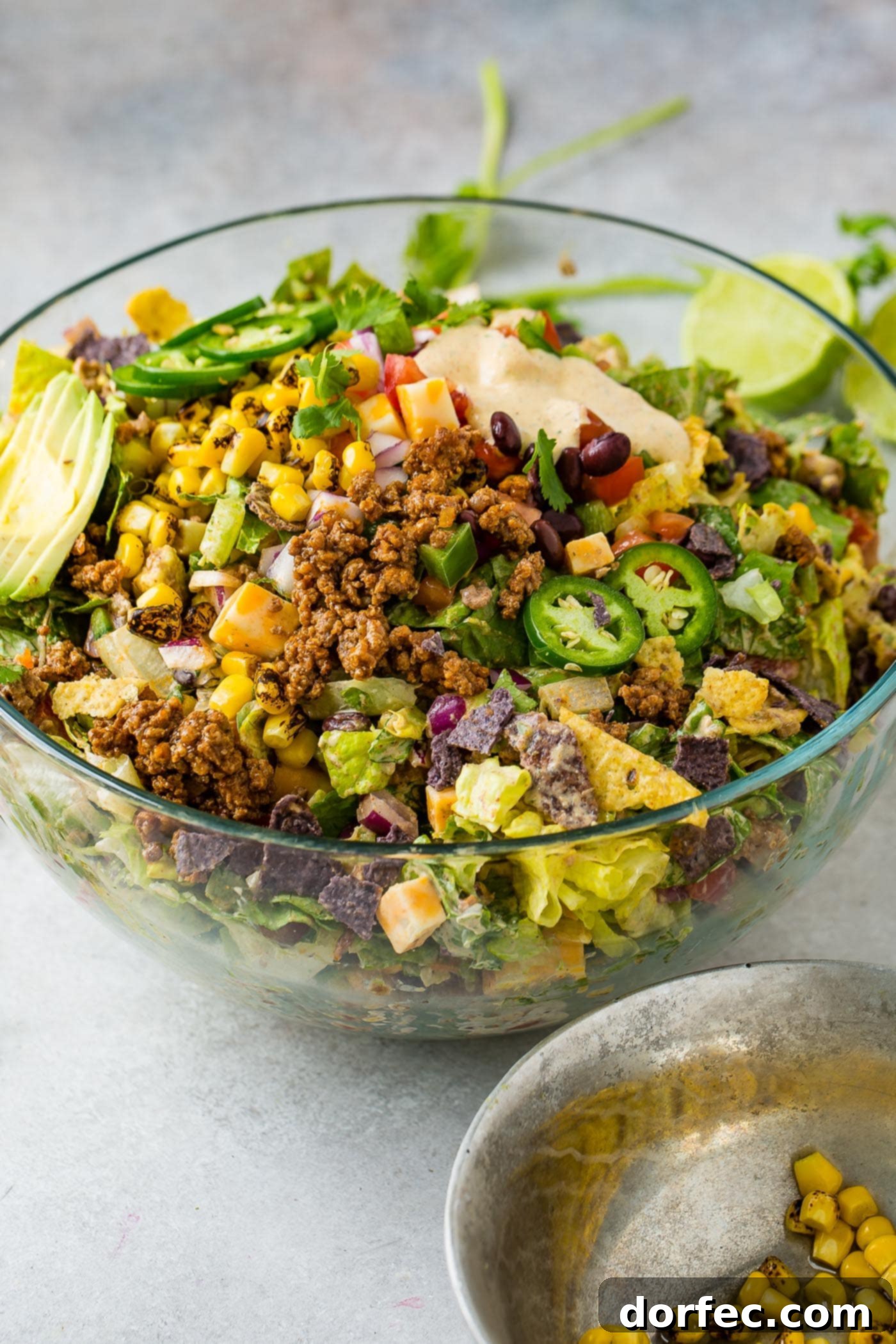 A large glass bowl of tex-mex taco salad. There are tomatoes, tomatillos, corn, beans, taco meat, chips and cheese in the salad. 