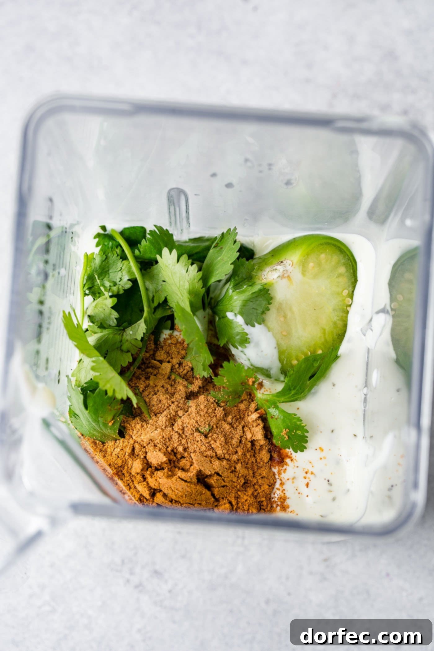 A blender with taco seasoning, cilantro, and ranch dressing ready to be mixed.