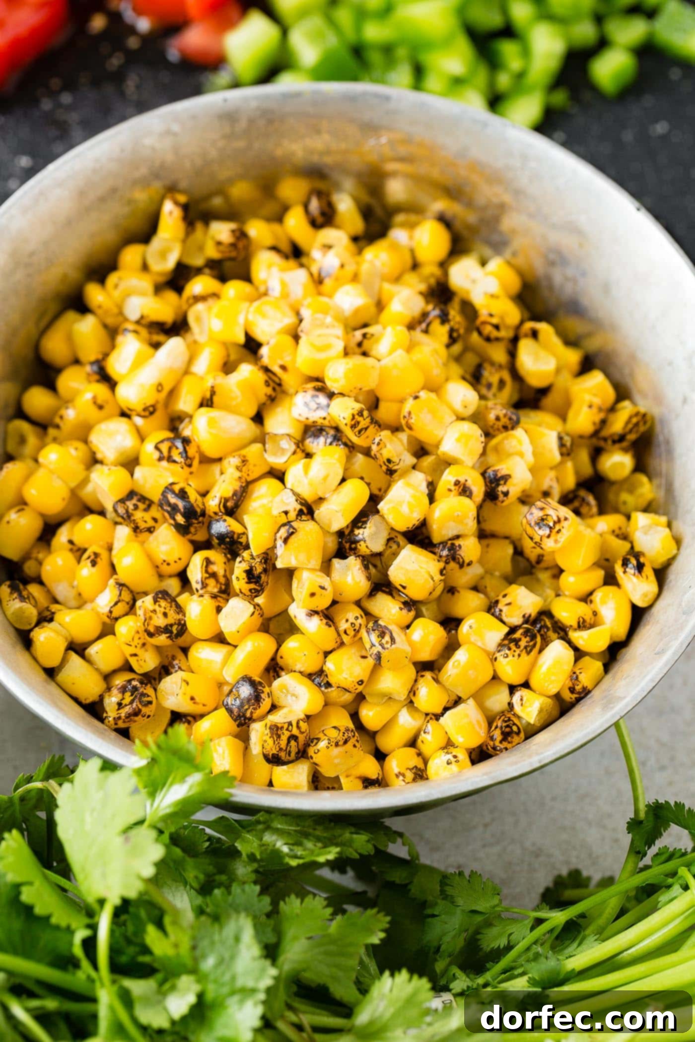 A bowl of roasted corn with cilantro leaves scattered around the bowl.