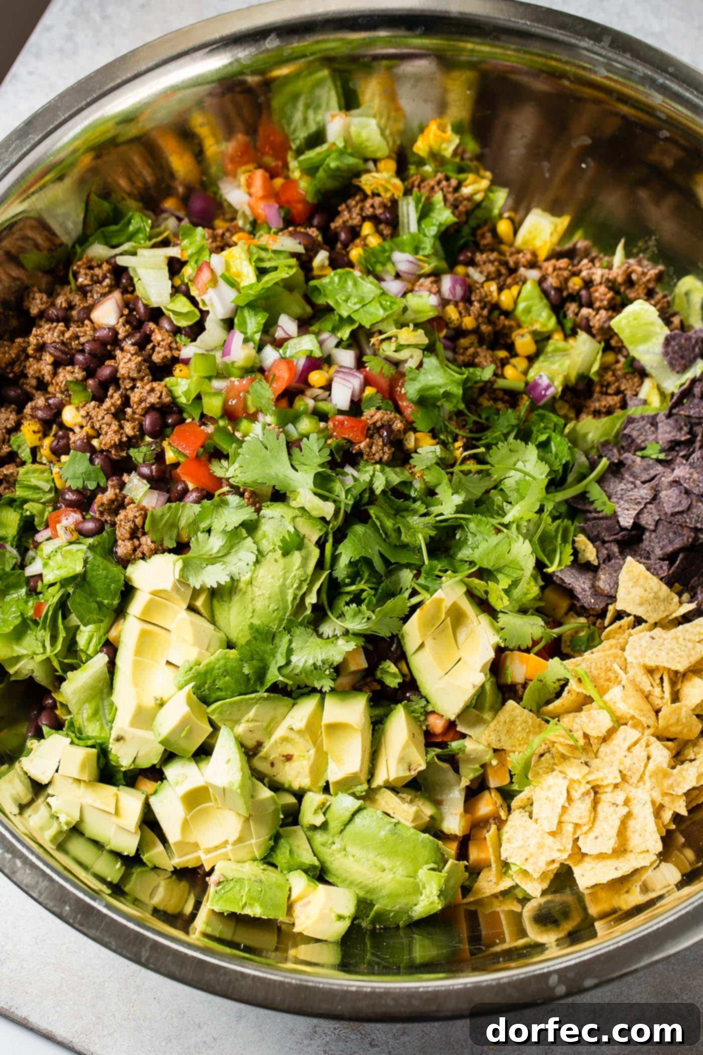 A close-up of tex-mex taco salad. You can see the fresh lettuce, tomatoes, corn, chips, and taco meat.