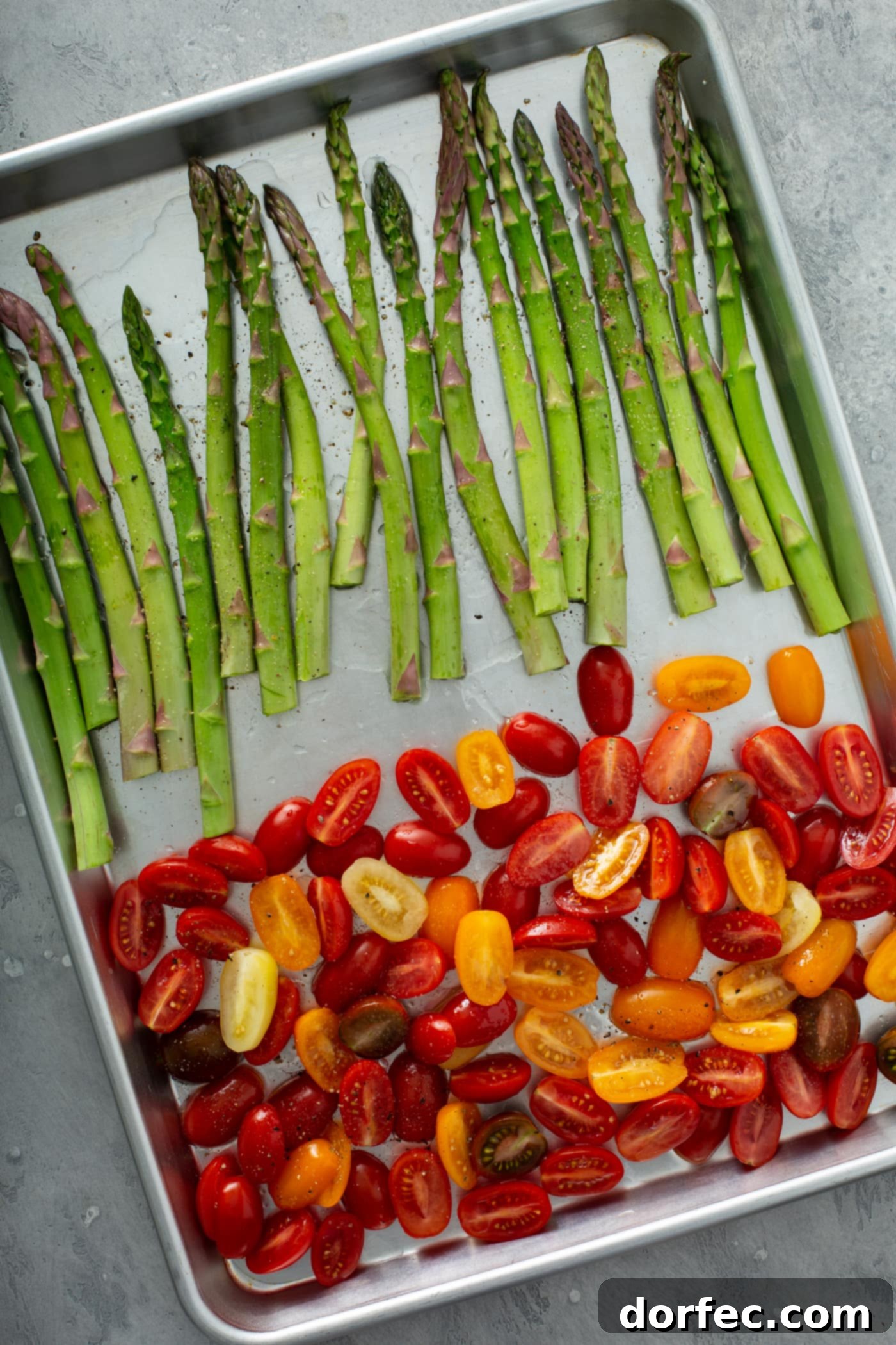 Glossy Balsamic Roasted Tomatoes and Asparagus 4 A baking pan holds neatly arranged fresh green asparagus on one end and colorful sliced red and yellow heirloom tomatoes on the other. The vegetables are lightly coated, ready for roasting to create a flavorful balsamic glazed side dish.