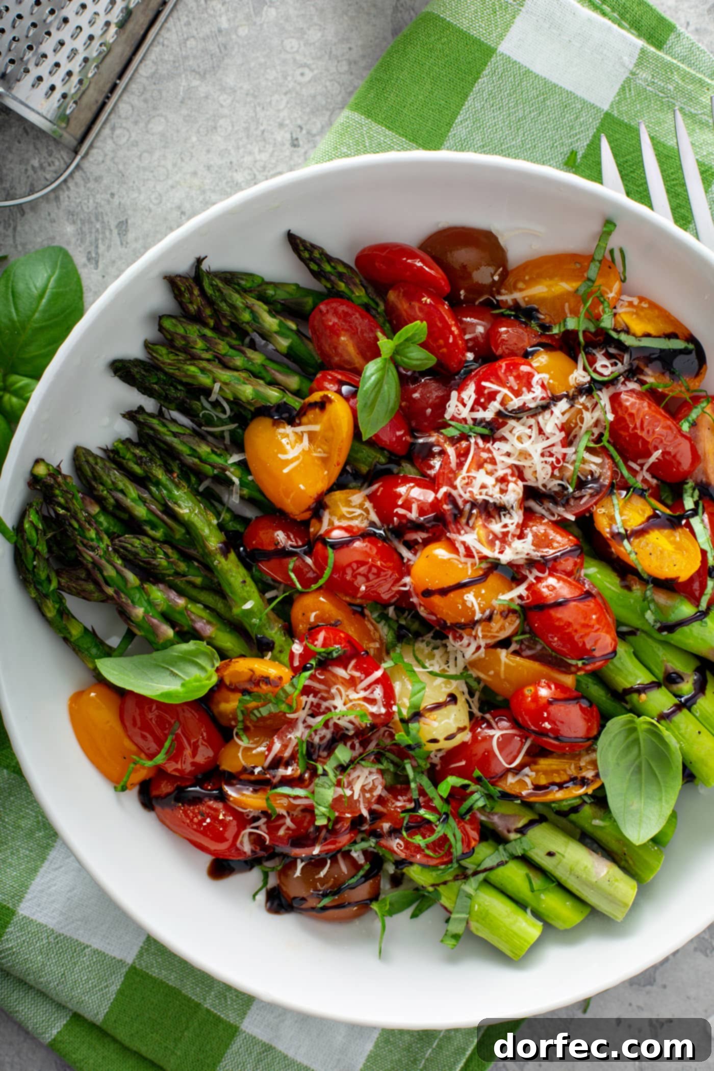 Glossy Balsamic Roasted Tomatoes and Asparagus 5 A serving dish filled with balsamic glazed roasted tomatoes and asparagus. The bright green, tender asparagus spears are covered with luscious, sliced red and yellow tomatoes, all glistening with a rich balsamic glaze. A delicate sprinkling of grated Parmesan cheese adds a final savory touch. The dish rests on a charming green and white checked cloth, ready to be enjoyed.
