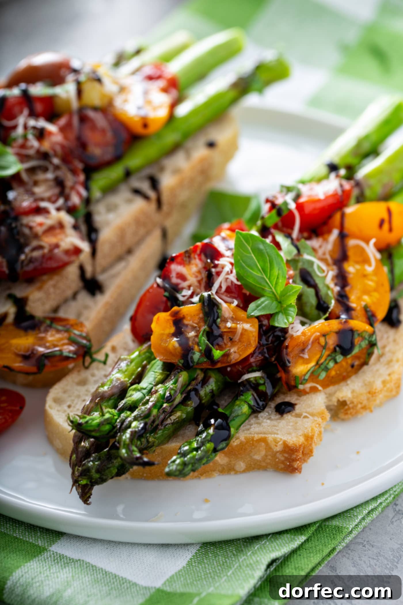 Glossy Balsamic Roasted Tomatoes and Asparagus 6 A delectable serving of balsamic glazed roasted tomatoes and asparagus artfully arranged on a slice of golden-brown toasted bread. The tender roasted vegetables are glistening with balsamic glaze and generously sprinkled with grated Parmesan cheese. In the background, another serving on two slices of bread awaits, highlighting this dish's versatility.