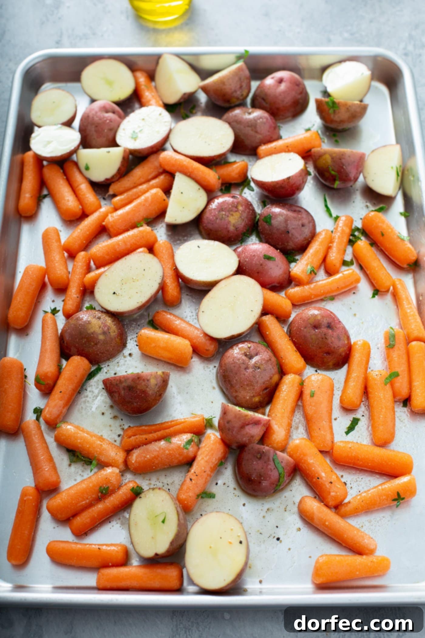 A sheet pan loaded with halved red potatoes and uniform baby carrots, perfectly prepped for roasting.