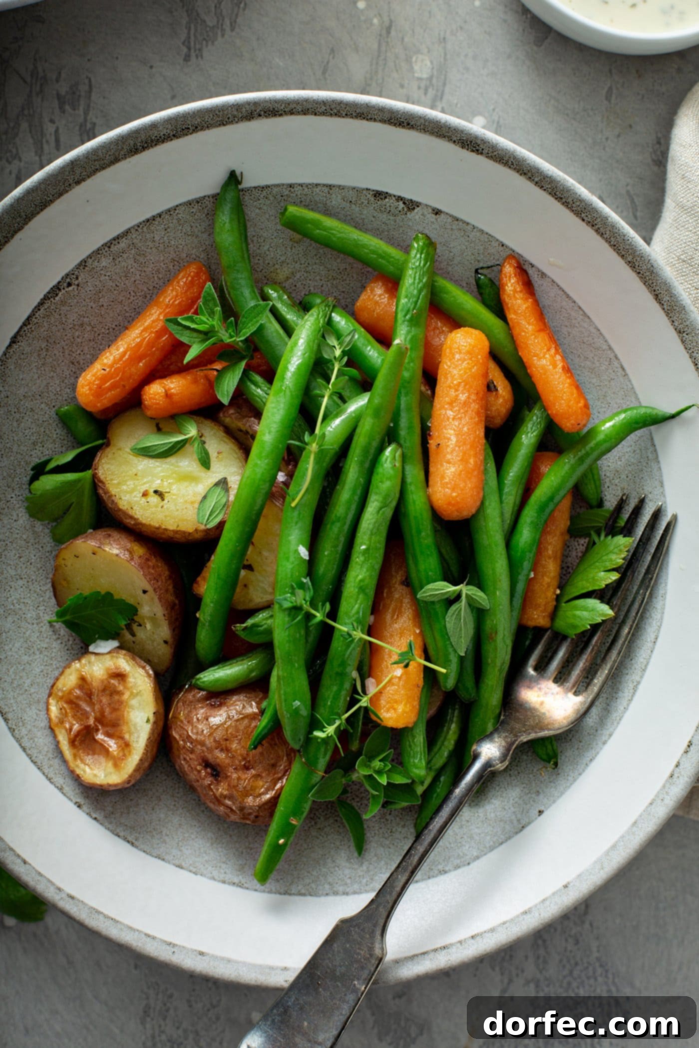 A dinner plate showcasing a colorful medley of roasted potatoes, carrots, and green beans, generously sprinkled with fresh herbs. A fork rests on the plate, ready to enjoy the meal.