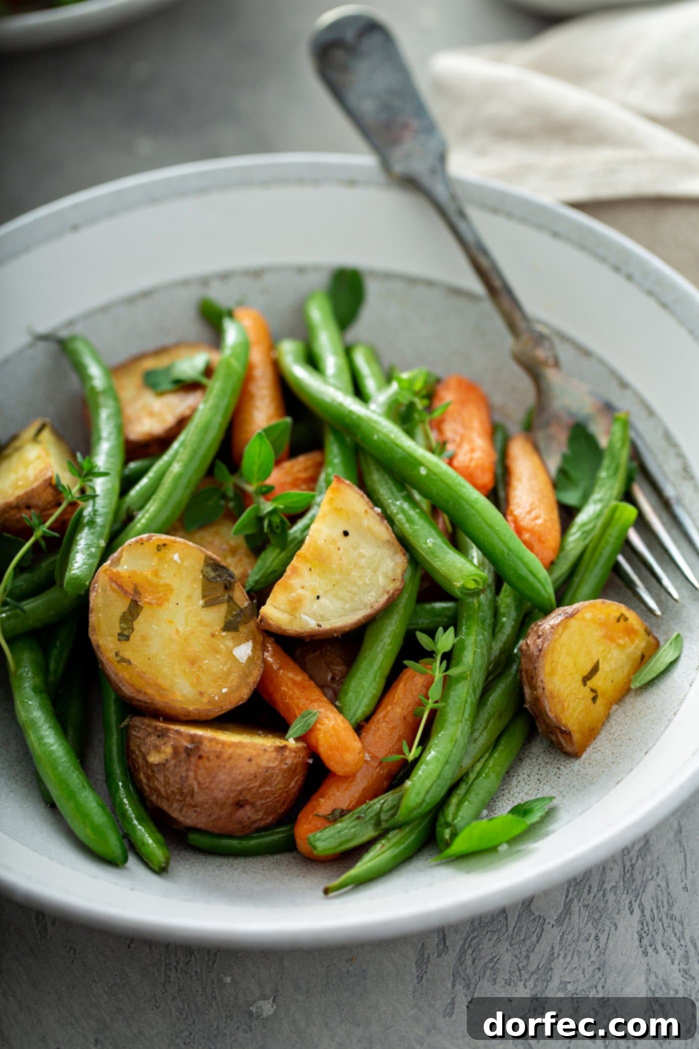 A plate generously filled with perfectly roasted red potatoes, tender baby carrots, and crisp fresh green beans. A fork is positioned next to the roasted vegetables, inviting enjoyment.