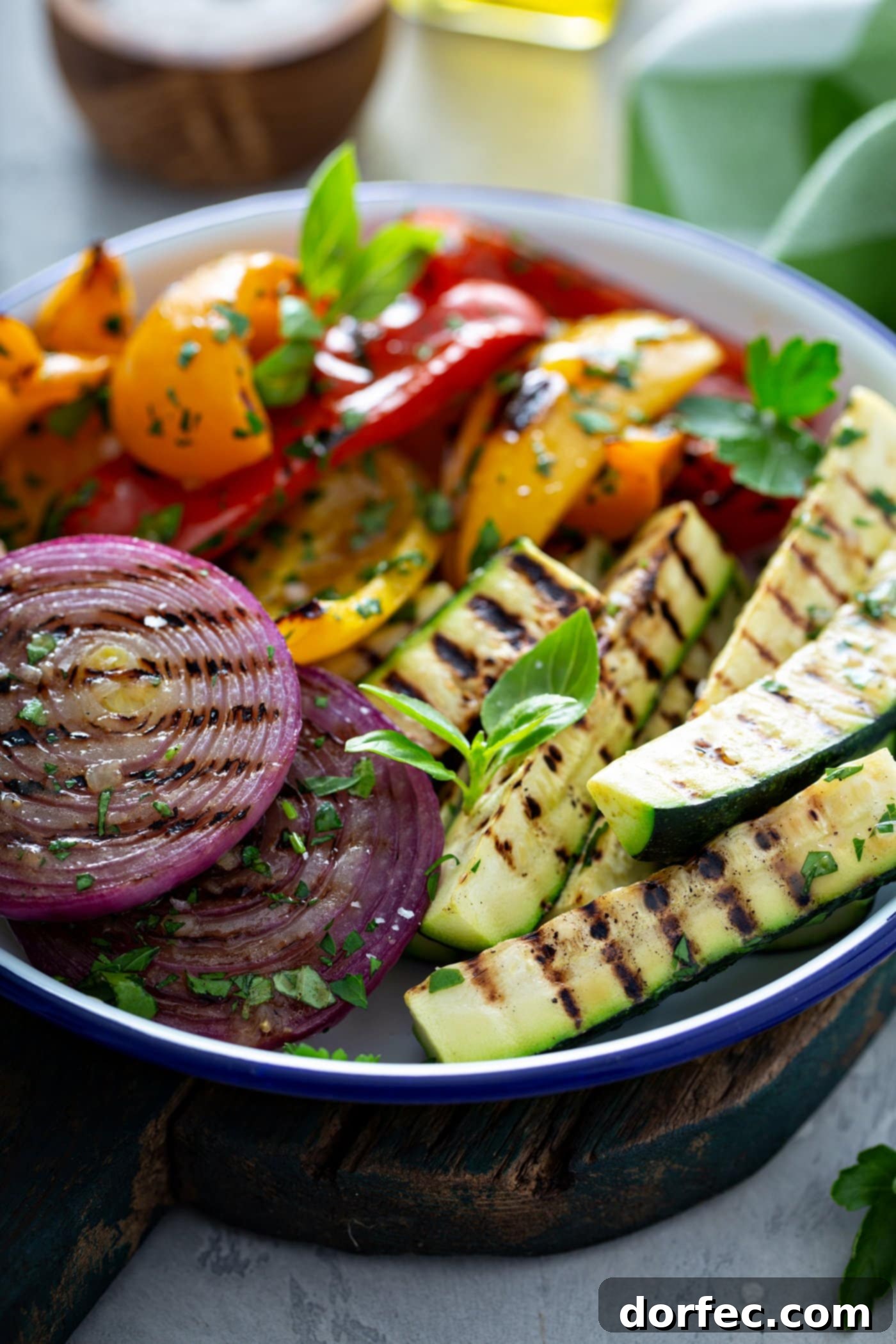 A serving dish of grilled veggies. The zucchini wedges, sliced red onions, and red and yellow bell peppers have perfect grill marks. and the veggies have a few parsley leaves scattered on top.