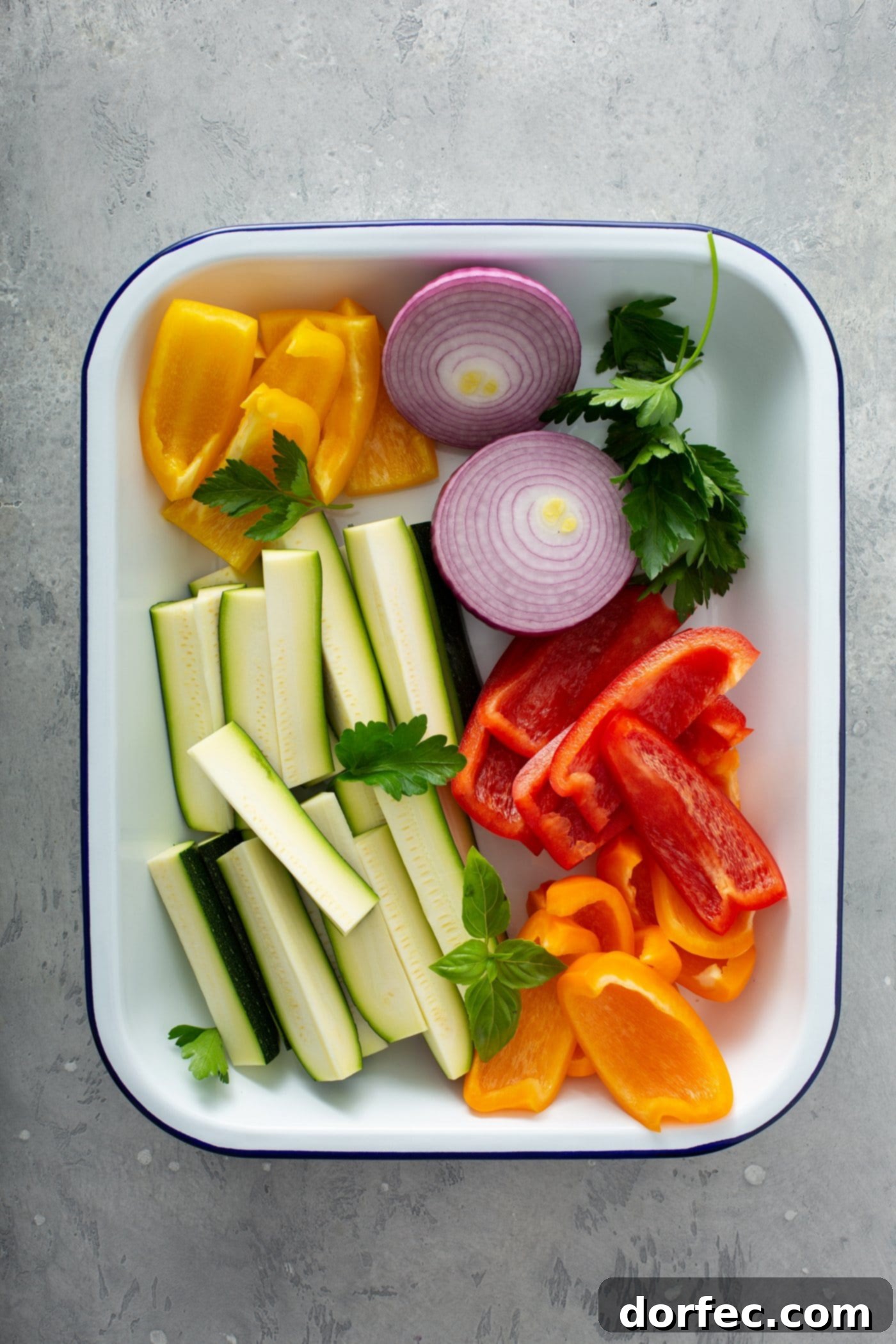 A plate with fresh zucchini wedges, sliced red onion, slices of red and yellow bell peppers, and parsley leaves.