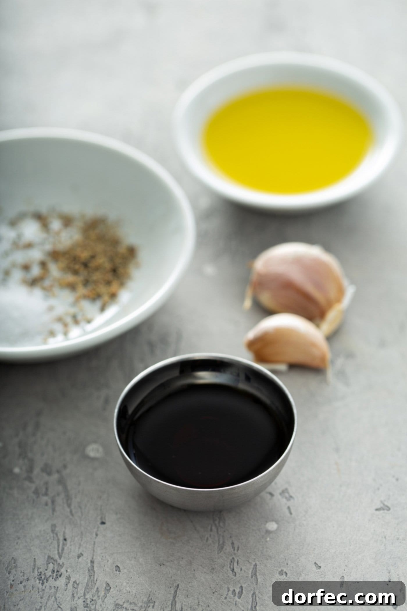 Small containers of spices, balsamic vinegar, oil and two cloves of garlic.