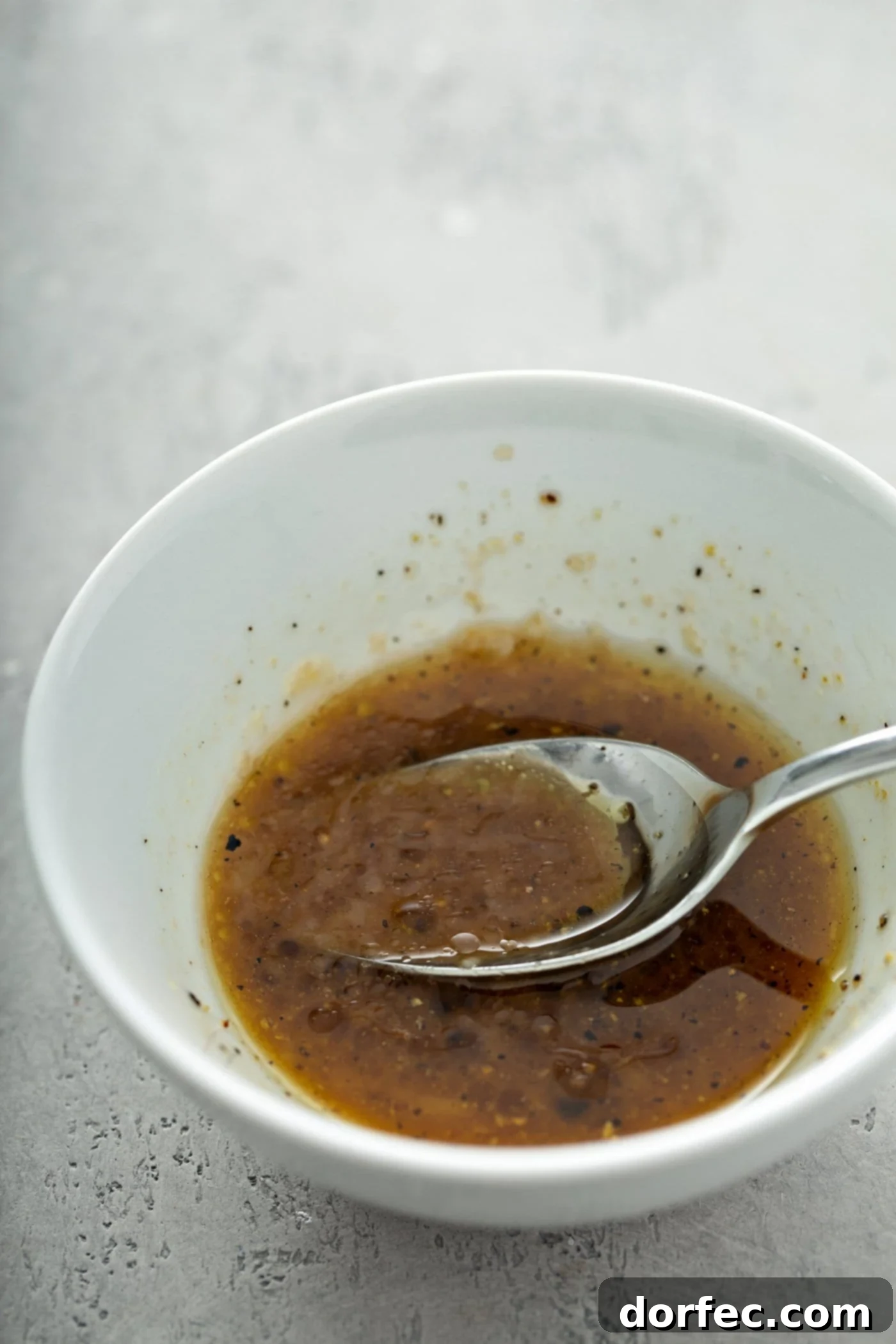 A white bowl containing balsamic glaze. There is a spoon in the bowl.