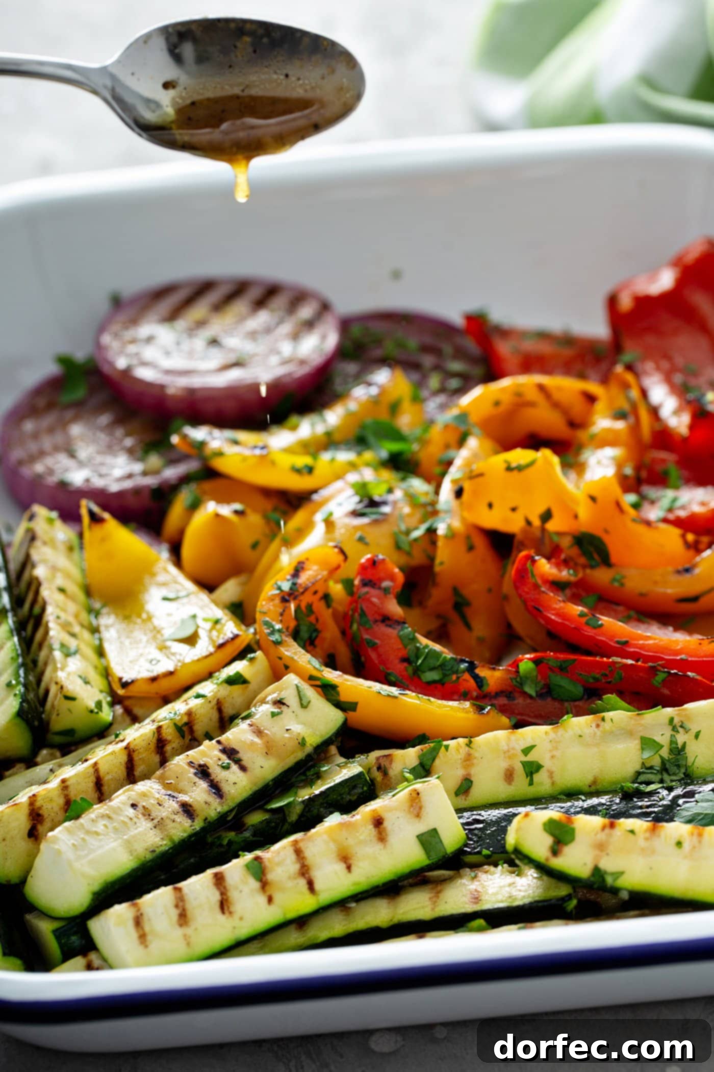 A serving dish filled with grilled veggies. The sliced red onion, zucchini wedges and red and yellow bell peppers have wonderful grill marks and there are parsley leaves scattered on top of the veggies.