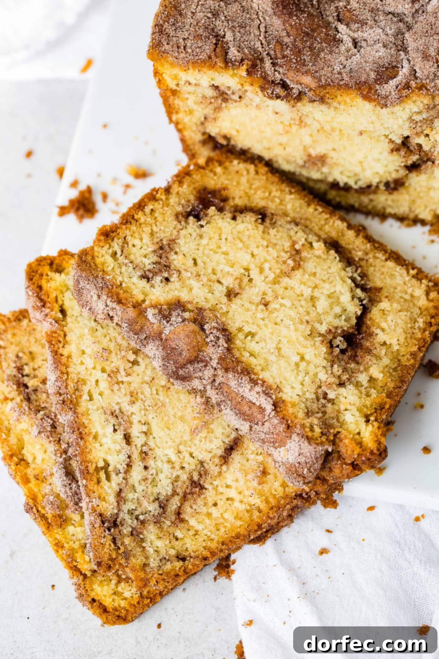 Cinnamon Sugar Swirl Loaf 3 Three perfectly cut slices of Snickerdoodle Bread resting on a plate, with the remainder of the loaf visible in the soft-focus background, highlighting the golden crust and cinnamon swirl.
