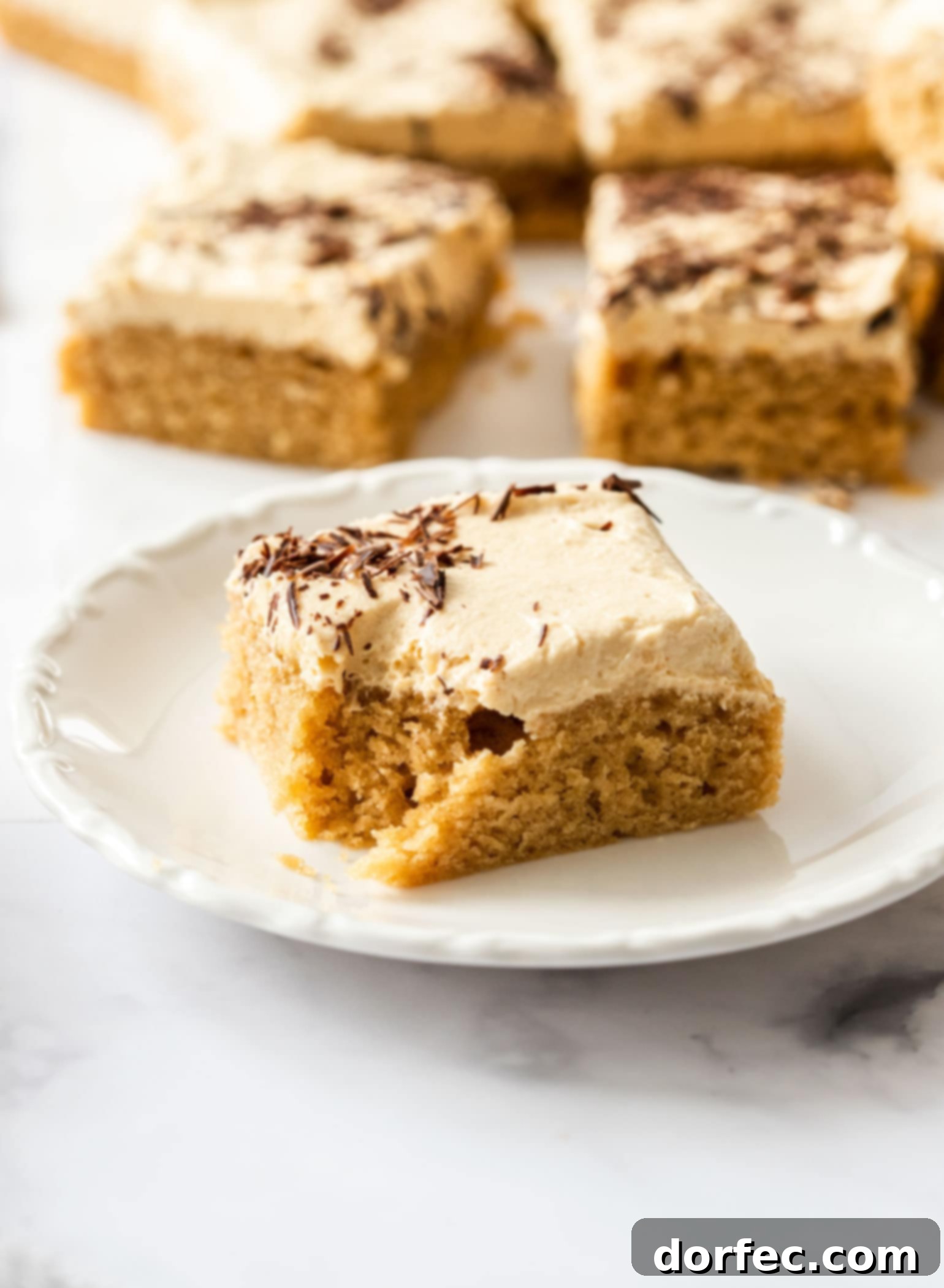 Ultimate Peanut Butter Sheet Cake 7 A single, perfectly cut slice of Peanut Butter Sheet Cake sits elegantly on a white saucer, ready to be enjoyed as a delightful individual serving.