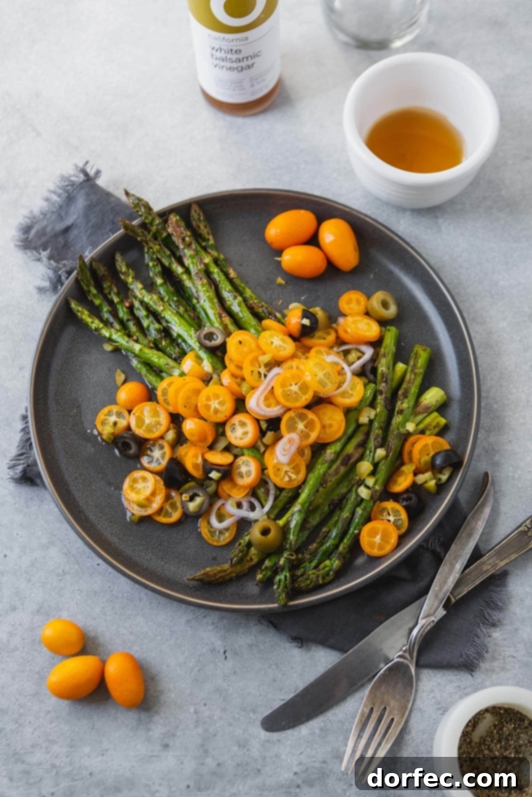 A closer view of the roasted asparagus and kumquat dish, highlighting the glistening olive oil dressing, the delicate texture of the asparagus tips, and the vibrant orange slices of kumquat, ready to be served.