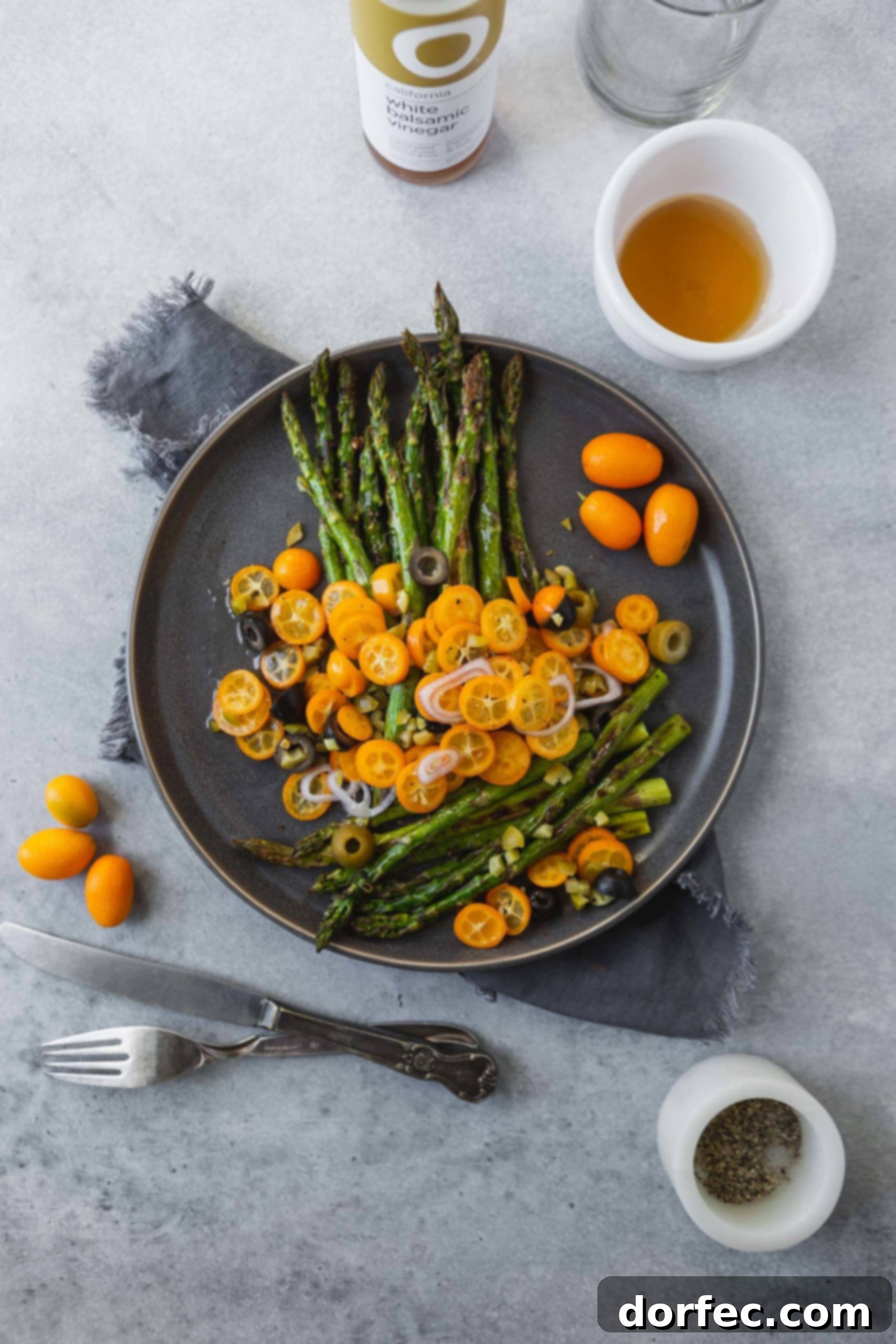 A beautifully presented serving of roasted asparagus with kumquats, olives, and shallots, glistening with dressing, ready to be enjoyed as a gourmet side dish.