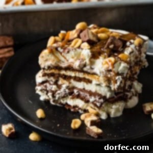 A square piece of Snickers Ice Cream Cake is captured in a delectable close-up, showcasing its irresistible layers. Each layer is distinct: dark chocolate cookie from the ice cream sandwiches, creamy vanilla ice cream, rich hot fudge, sweet caramel sauce, fluffy whipped cream, and generous chunks of chopped Snickers bars. The top is garnished with additional hot fudge, caramel drizzles, and a sprinkle of crunchy salted peanuts, making it a perfect no-bake frozen dessert.