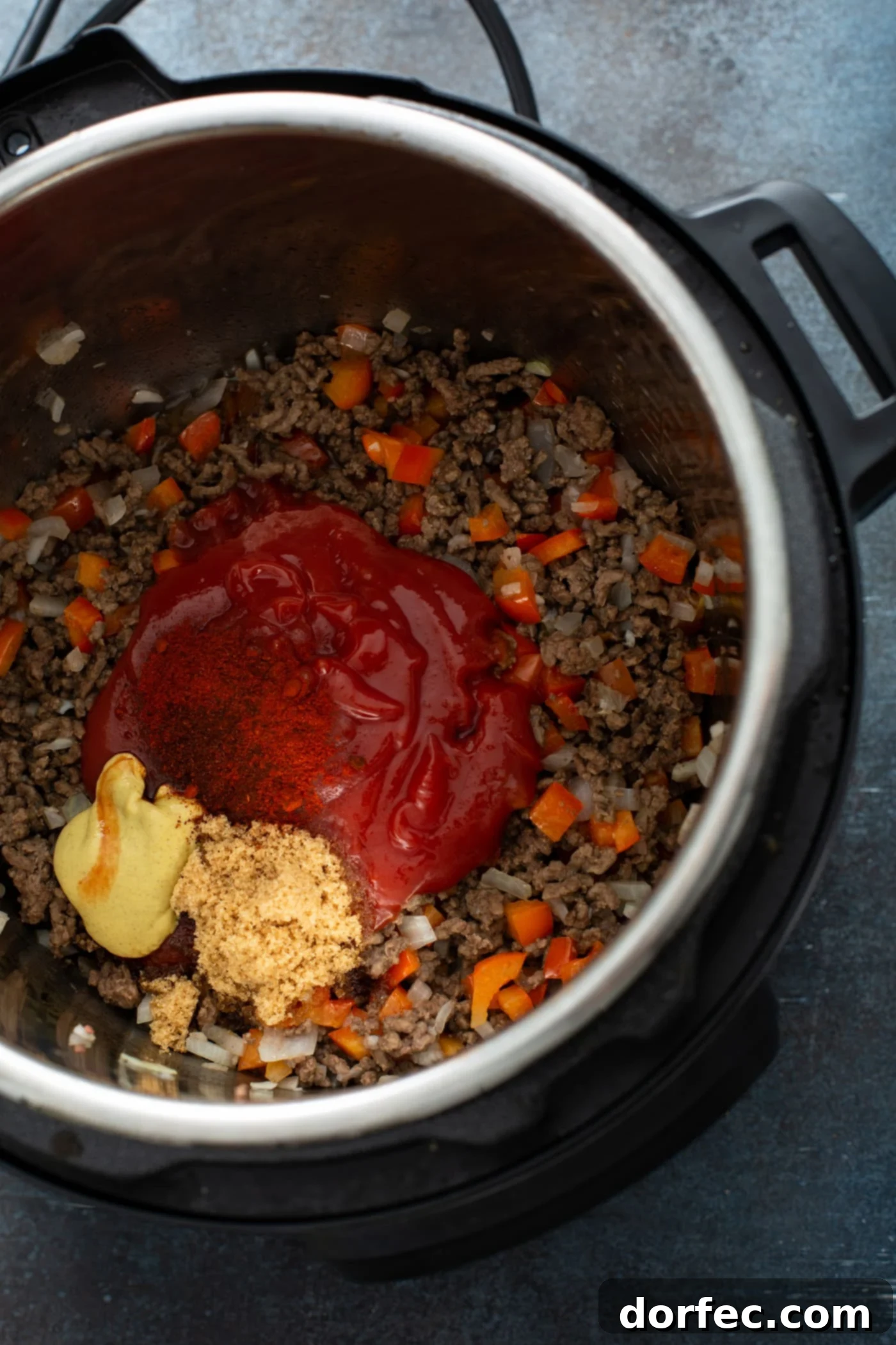 Instant Pot Sloppy Joes An instant pot with browned hamburger, chunks of red bell pepper, ketchup, dijon mustard and brown sugar.