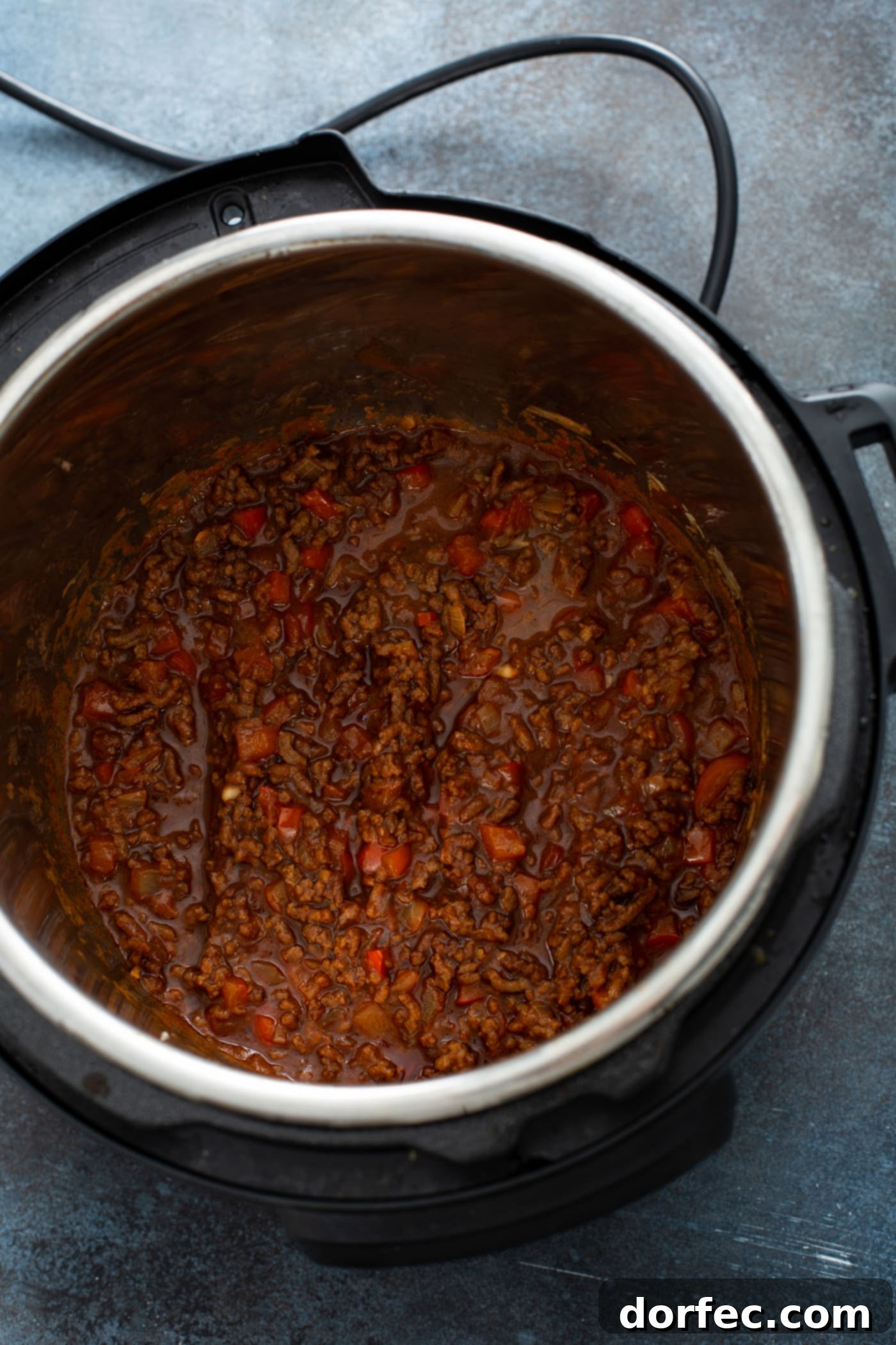 Instant Pot Sloppy Joes An instant pot with cooked sloppy joe filling in it. You can see the browned hamburger with chunks of red bell pepper and a thick sauce.