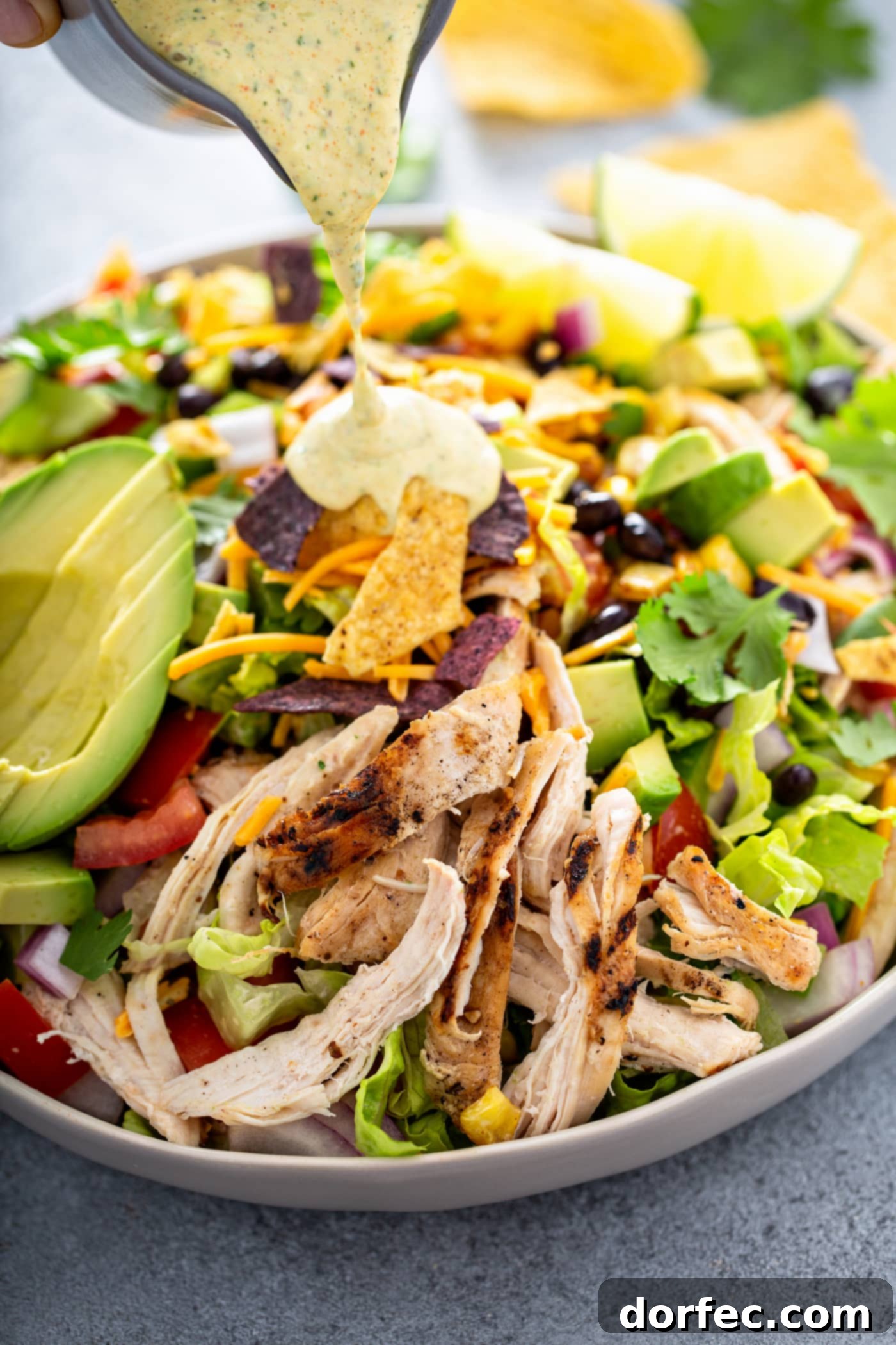 Simple Chicken Taco Salad A large bowl of chicken taco salad. There is shredded chicken, cheese, cilantro, beans, corn, tomatoes, red onions, peppers and sliced avocados. There are 2 lime wedges next to the salad and chips and dressing in the background.