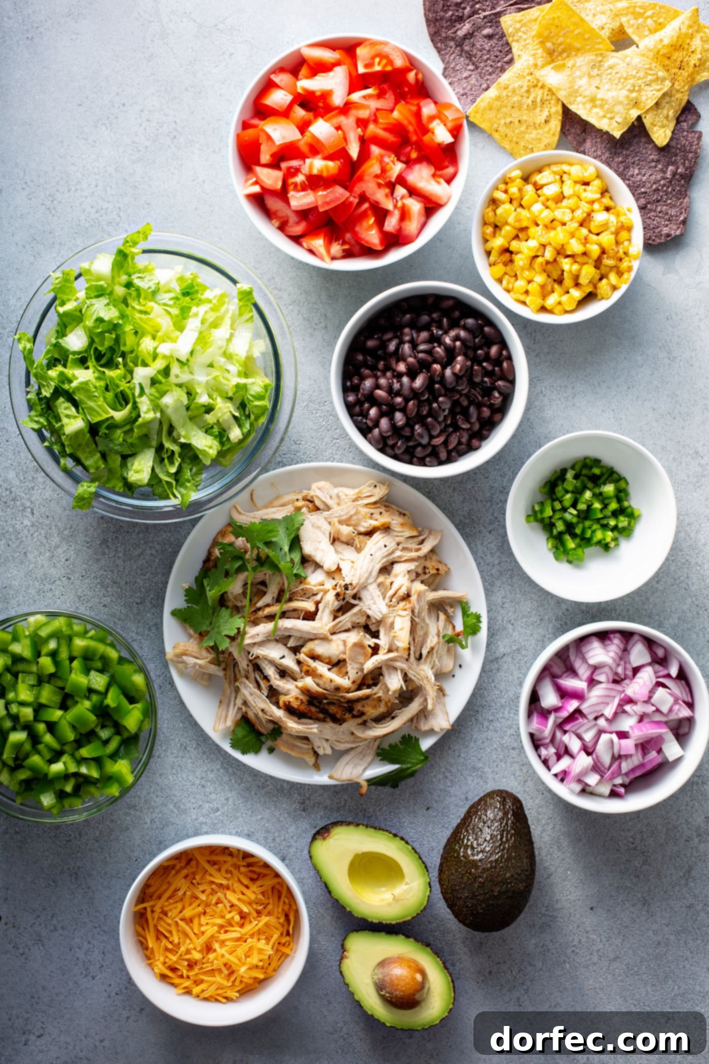 Simple Chicken Taco Salad Containers holding the ingredients for chicken taco salad. They contain corn, red onions, chicken, beans, bell peppers, taco seasoning, cilantro and there is an avocado on the table.