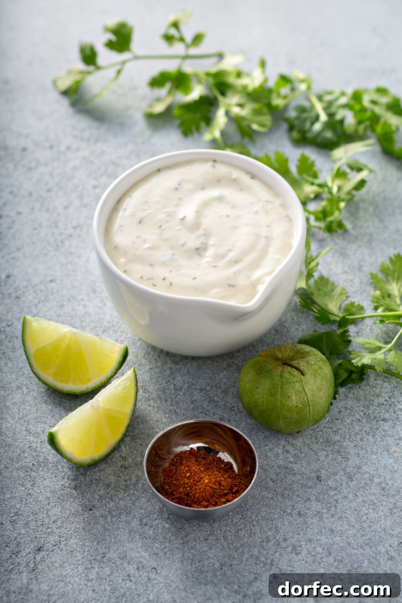 Simple Chicken Taco Salad Ingredients for chicken taco salad. A measuring cup with ranch dressing, 2 lime wedges, a tomatillo, taco seasoning, and fresh cilantro.