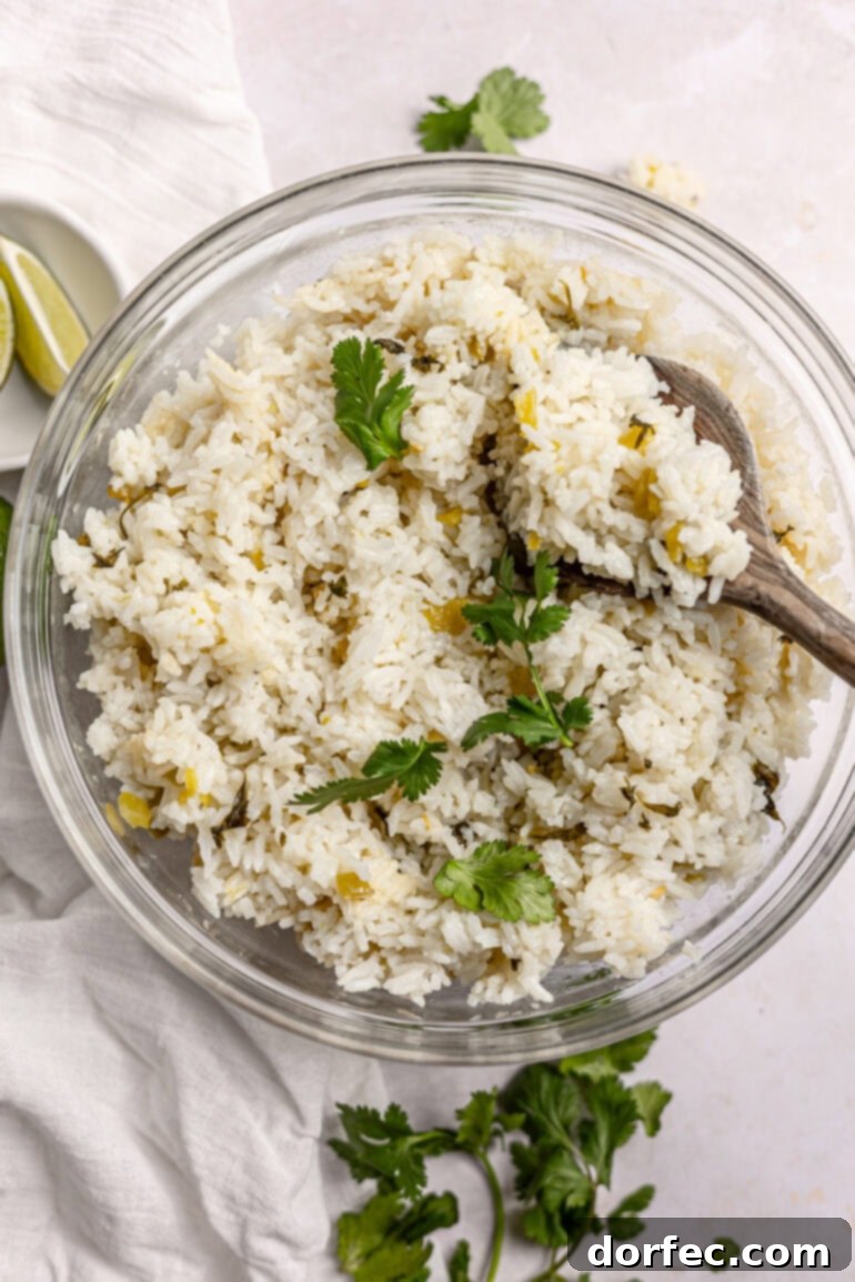 A large glass serving bowl full of fluffy cilantro lime rice, with a wooden spoon scooping up a serving, showcasing its readiness to be enjoyed.