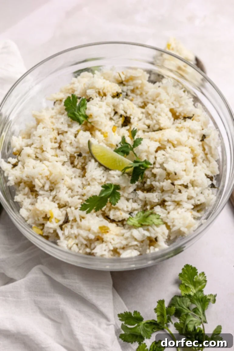 A close-up photo of a large glass serving bowl overflowing with perfectly cooked cilantro lime rice, garnished with fresh cilantro and a lime wedge, emphasizing its vibrant appeal.