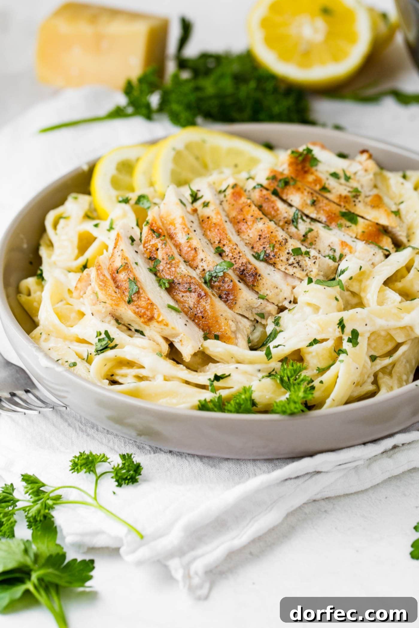 Chicken Fettuccine Alfredo A serving dish filled with chicken fettuccini alfredo. Sliced chicken is placed on top of the pasta and it is sprinkled with fresh parsley.