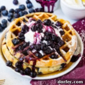 Golden Fluffy Blueberry Waffles 2 A stack of golden-brown blueberry waffles topped with fresh blueberries and whipped cream.