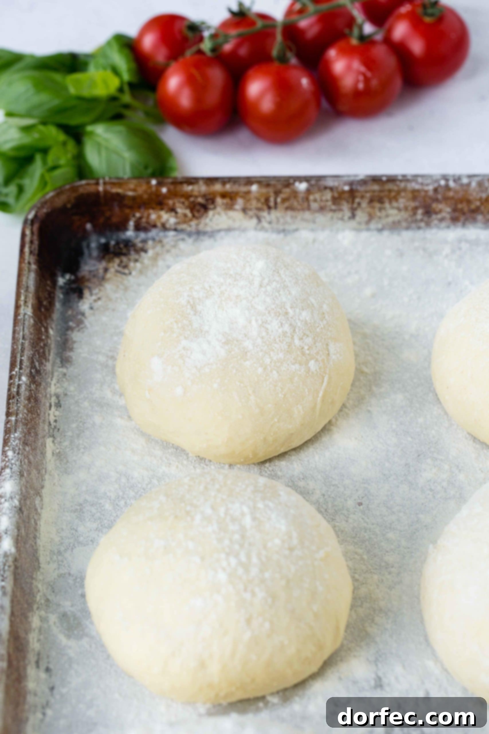 Four balls of pizza dough on a floured cookie sheet.