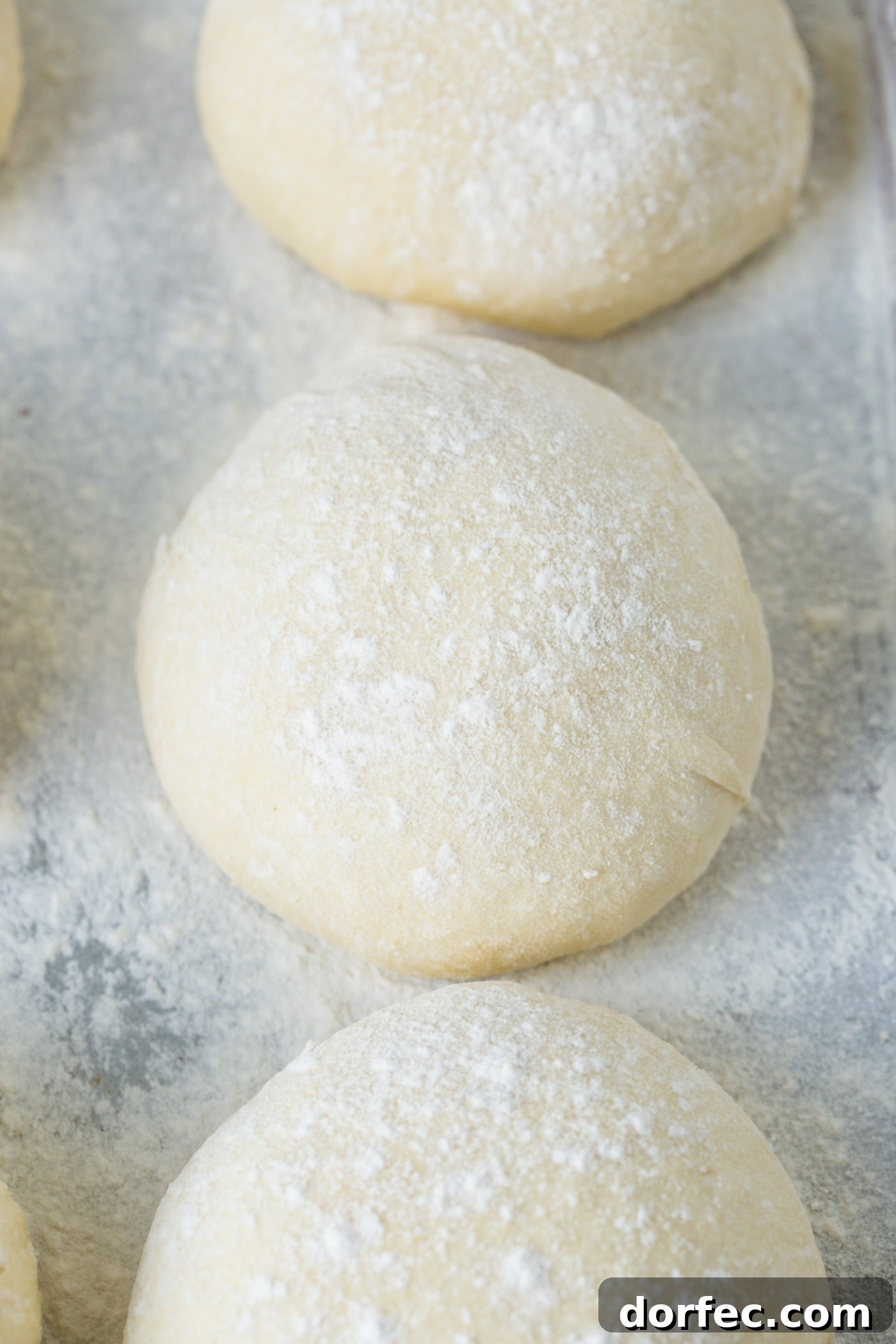 Three balls of pizza dough on a floured cookie sheet.
