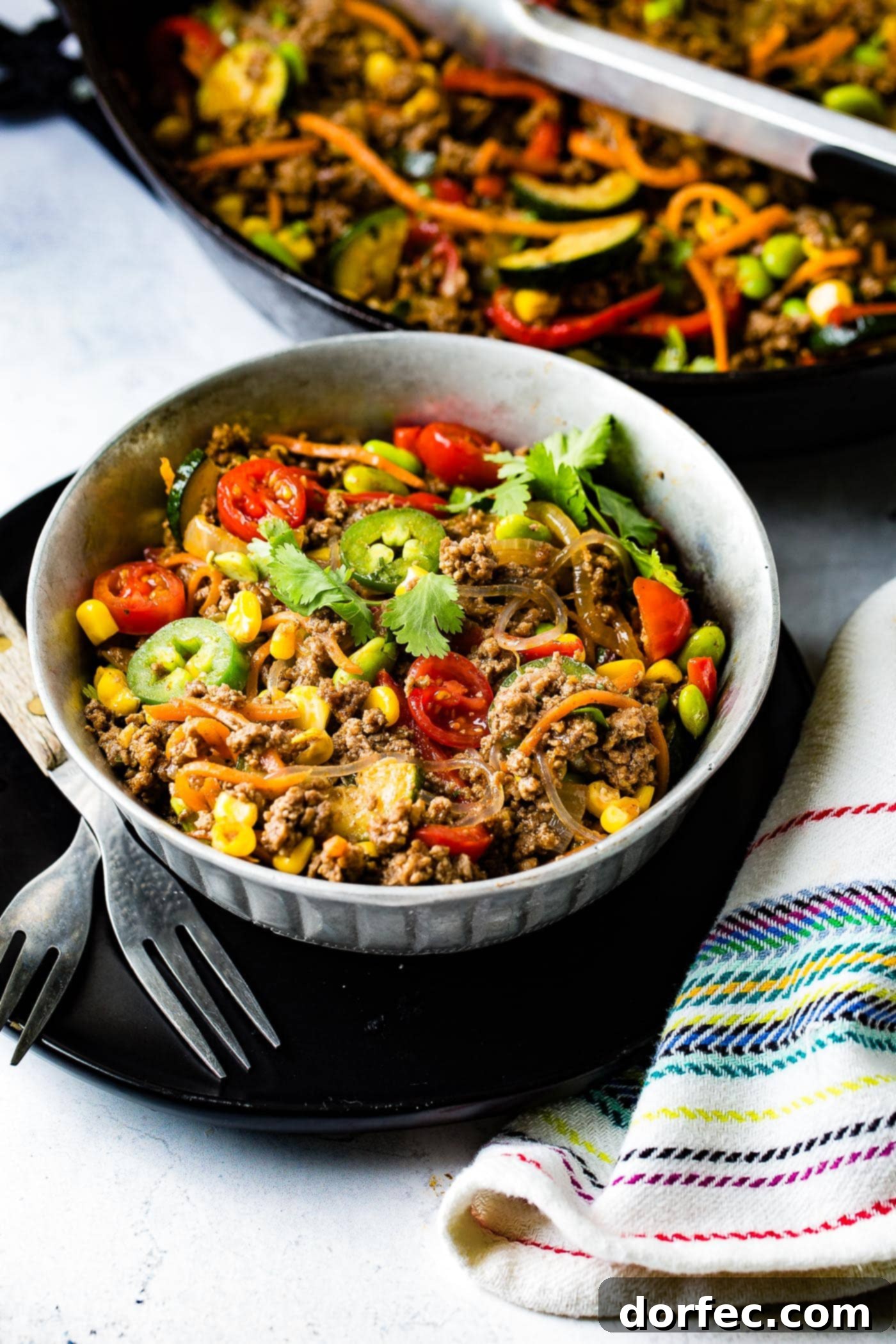 A bowl of taco pasta. The pasta contains corn, zucchini, jalapenos, tomatoes, pasta, and ground beef.