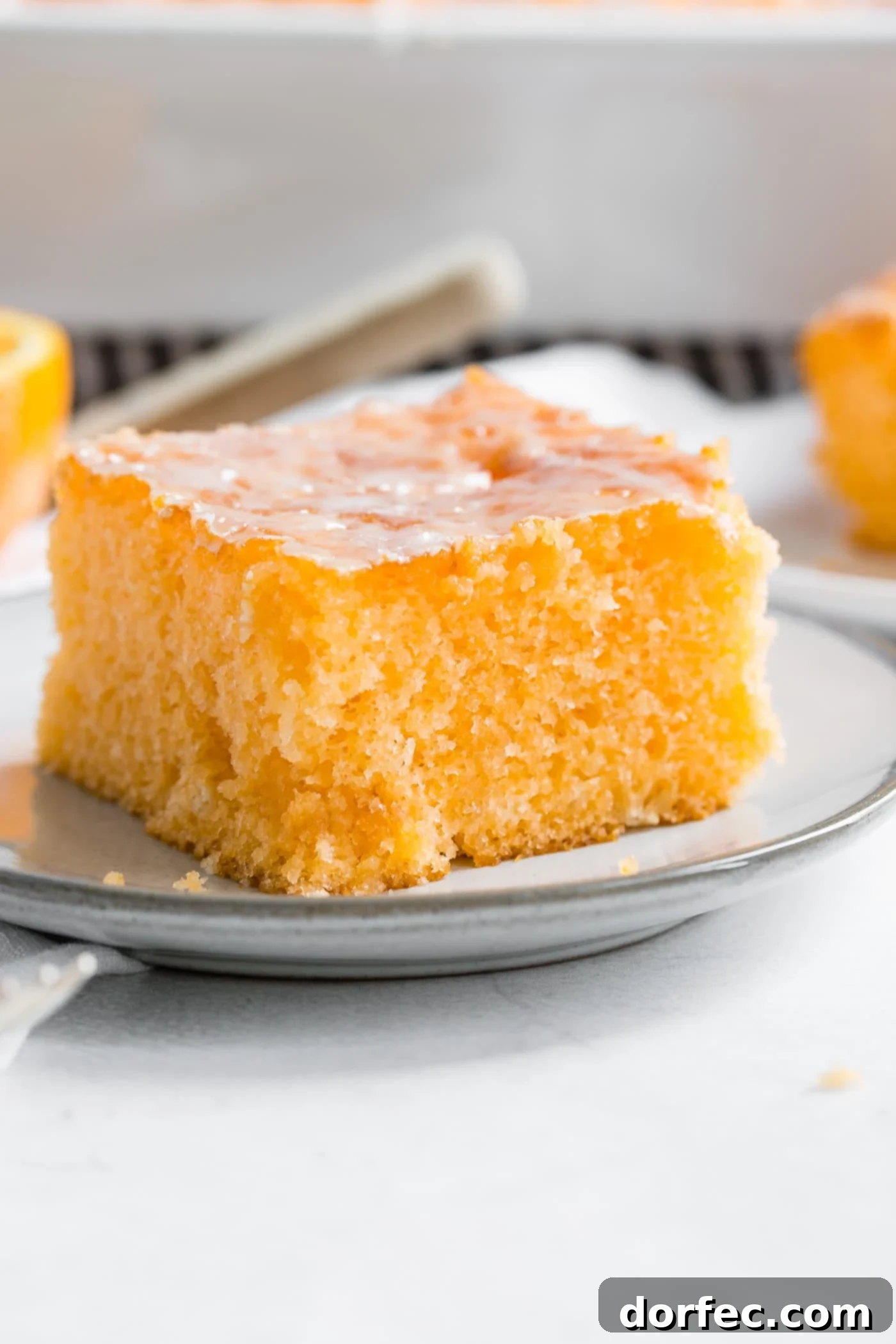 A photo of a piece of orange jello cake on a small white plate with orange glaze on the top, ready to be served.